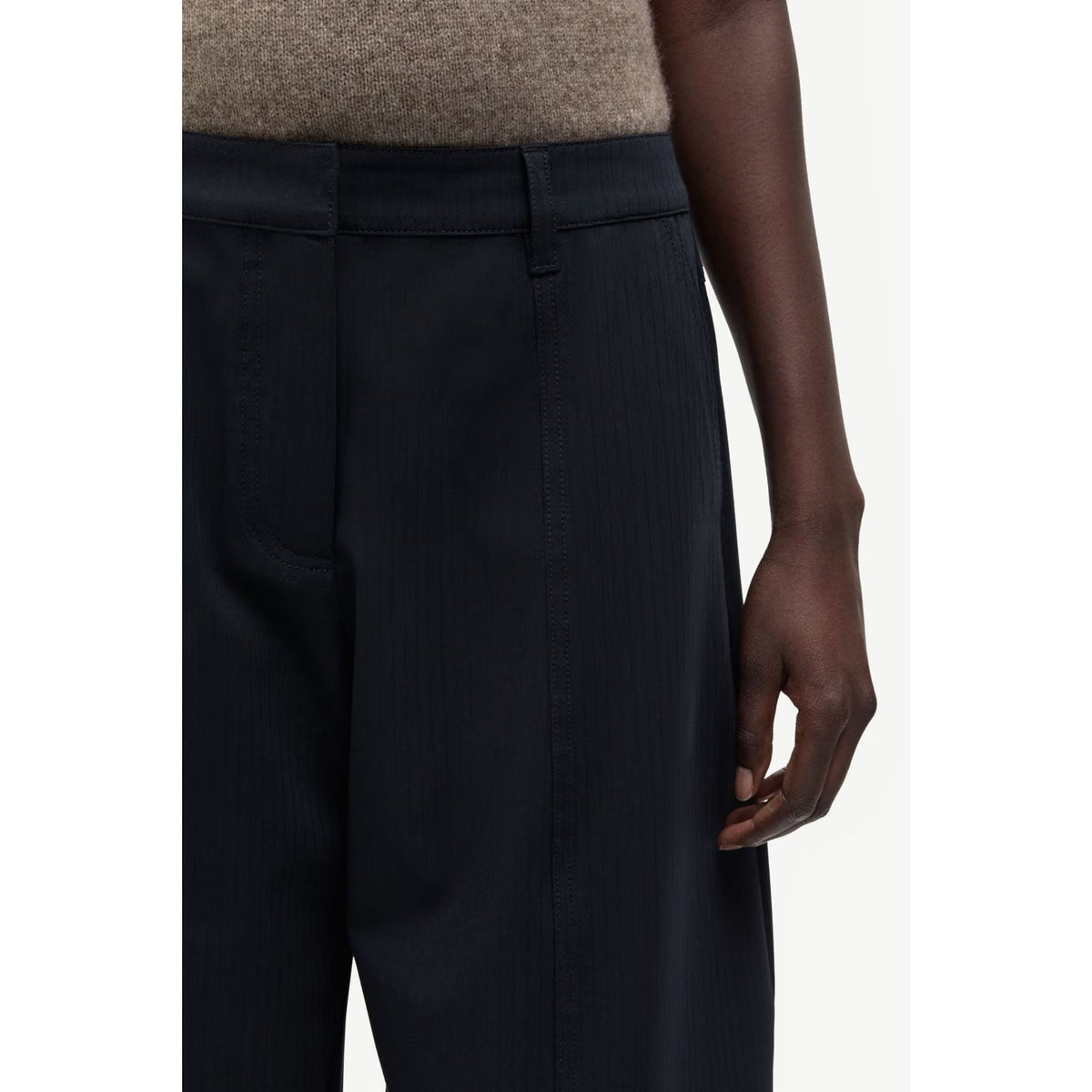 Close-up of a model wearing dark navy wide-leg trousers with a subtle vertical ribbed texture, paired with a beige knit top against a clean white background.