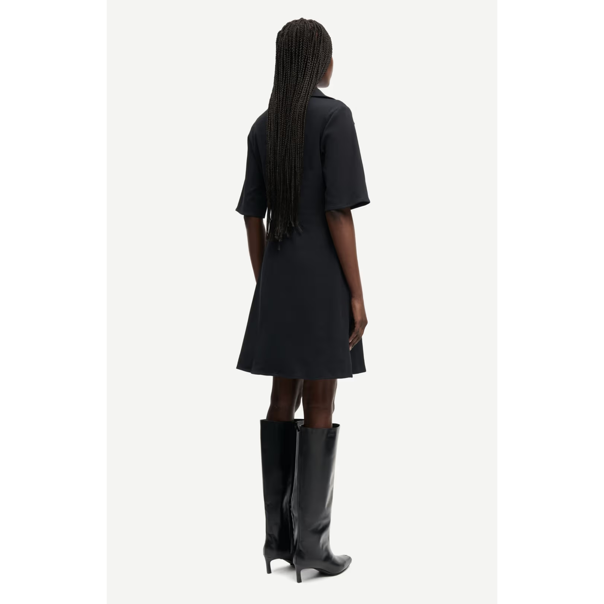 A model shown from the back wearing a black short-sleeve A-line dress and black knee-high boots against a light gray studio background.