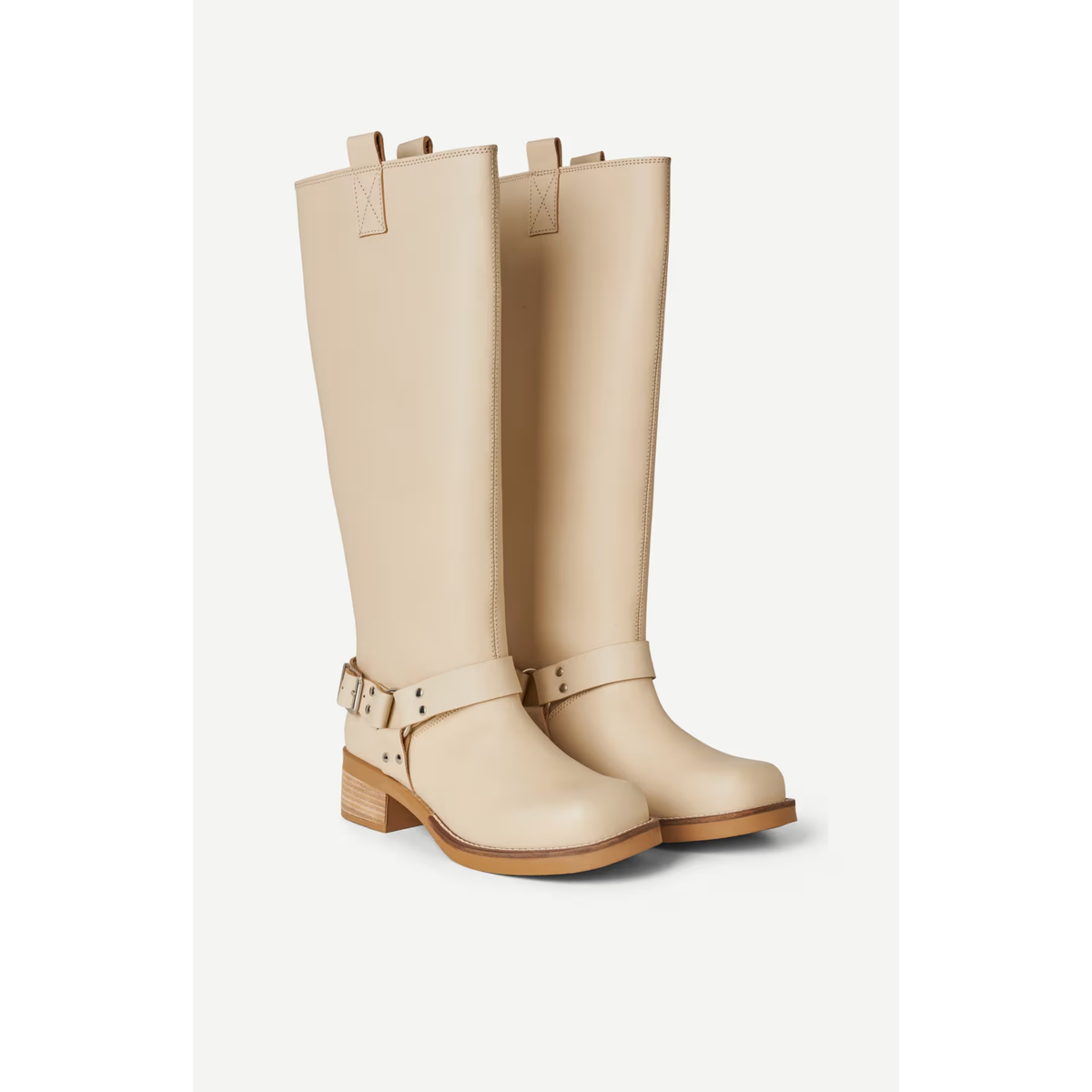 A pair of tall knee-high leather boots in a light beige color, featuring a buckle strap detail around the ankle and a low block heel, shown against a plain off-white background.