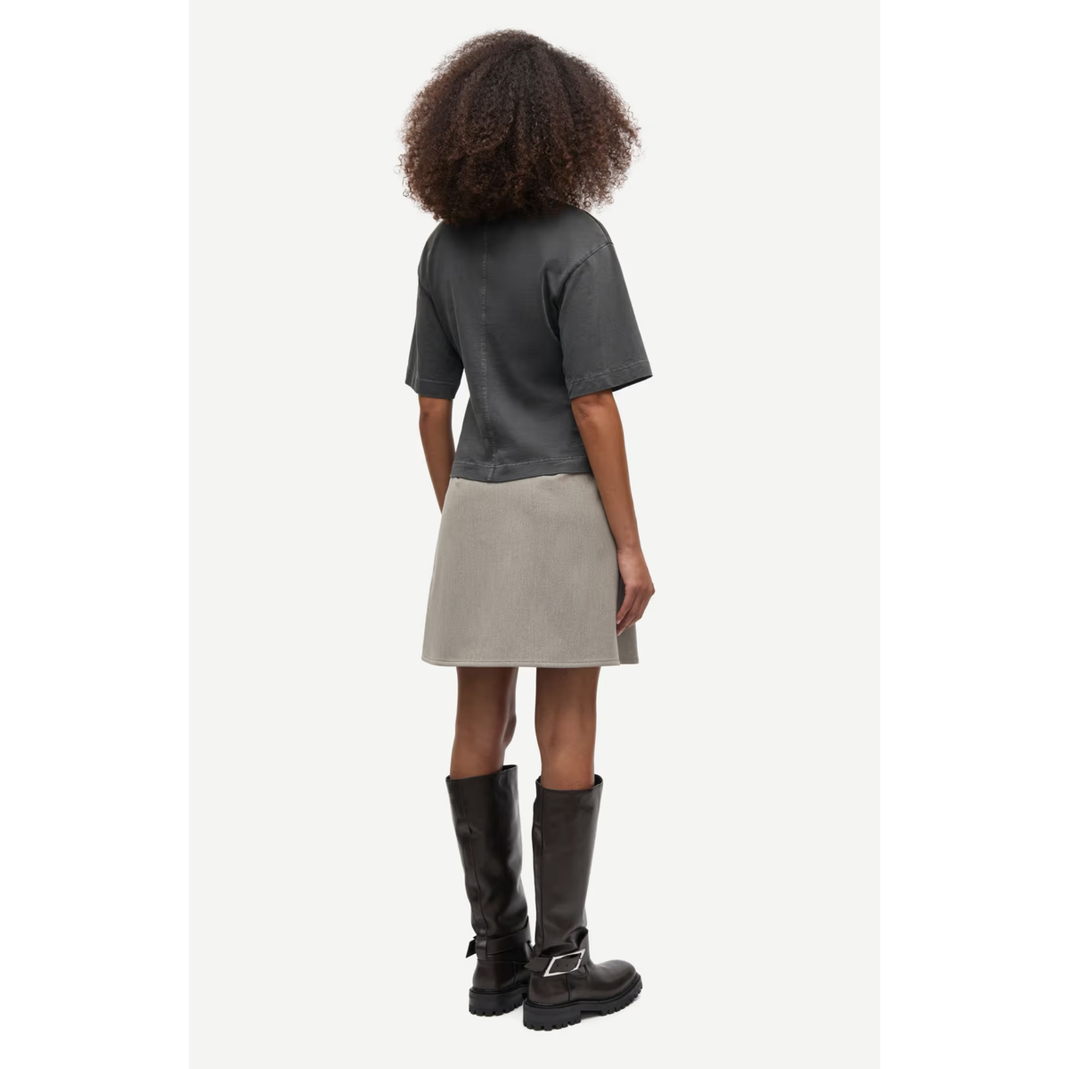 A model shown from the back wearing a dark gray short-sleeve top, a light gray A-line skirt, and black knee-high boots against a plain off-white background.