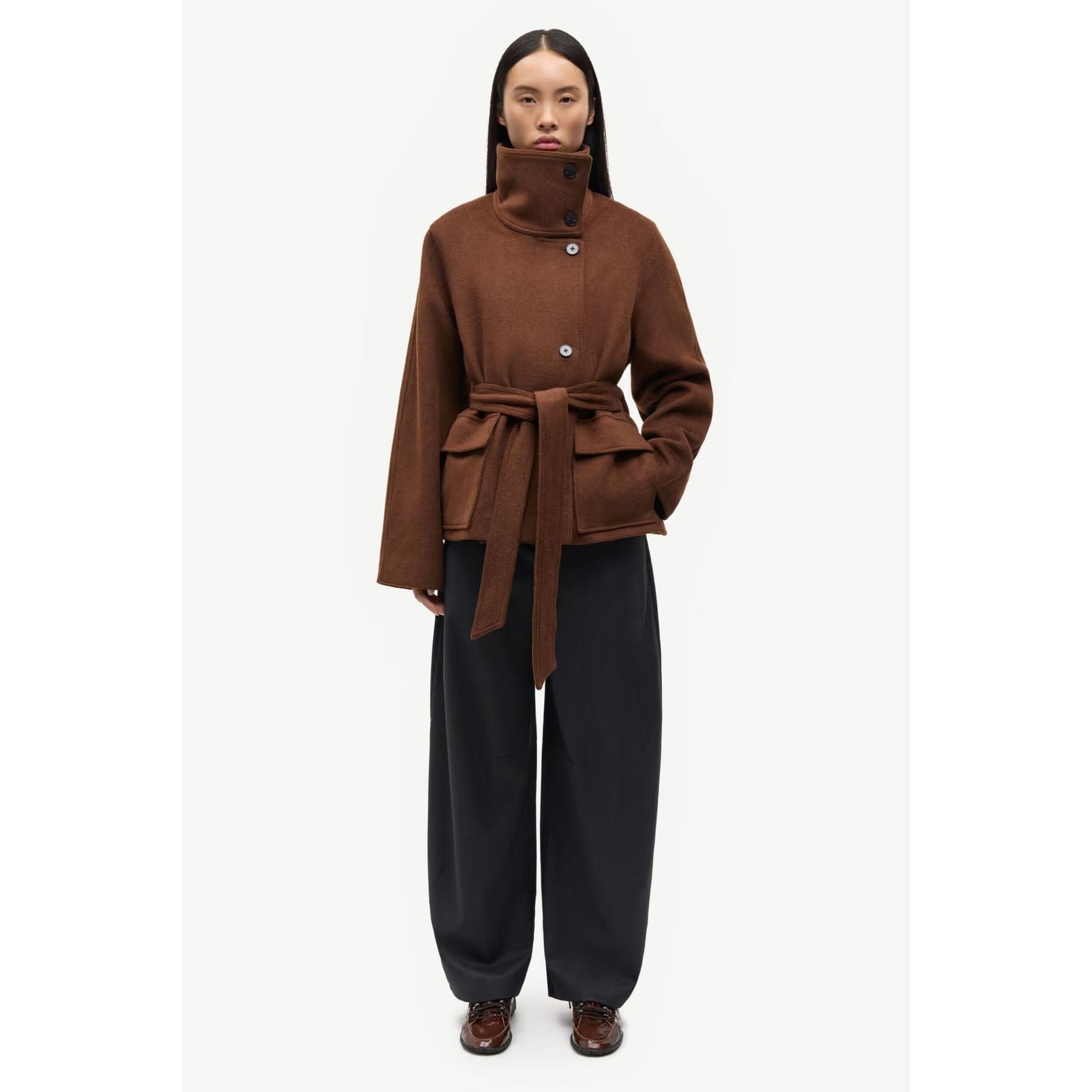 A brown wool-blend wrap coat with a high mock neck, asymmetrical button closure, and a matching waist tie belt, shown on a light gray background.