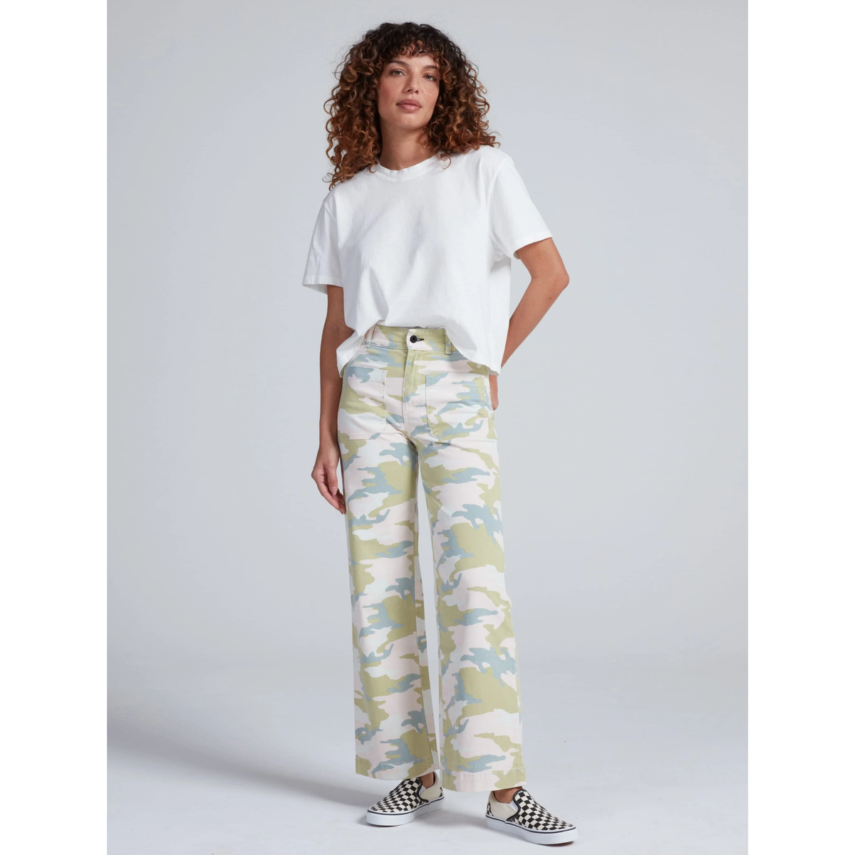 Woman wearing a white t-shirt and patterned pants on a gray background