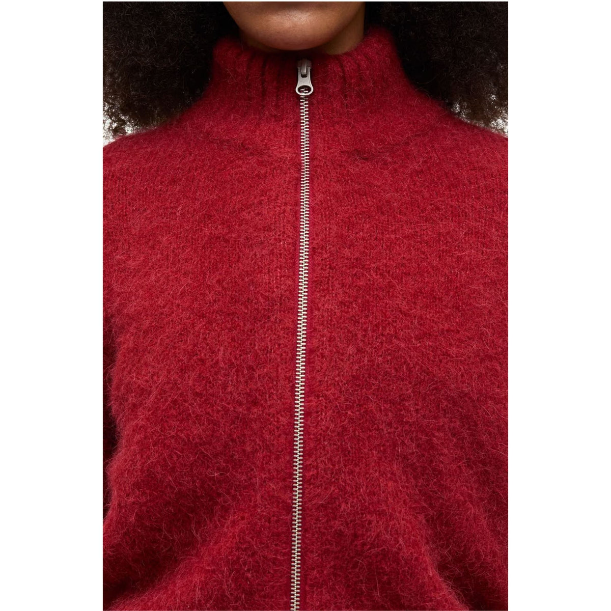 Close-up of a person wearing a fuzzy red zip-up sweater with a high ribbed collar and a silver zipper.