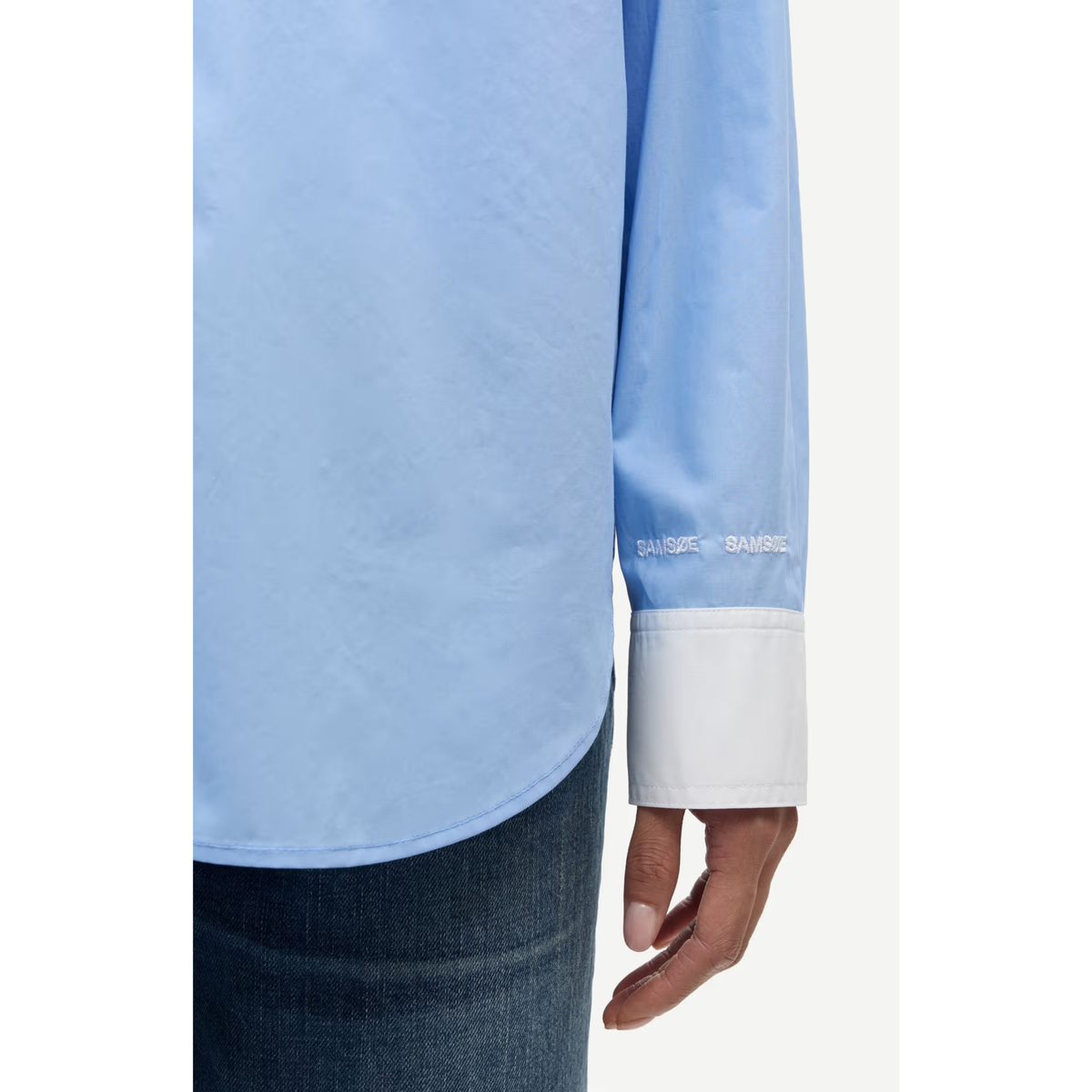 Close-up of a light blue long-sleeve dress shirt with a white cuff, worn by a model with dark blue jeans. The brand name 'BAUSSE' is embroidered in white on the cuff.