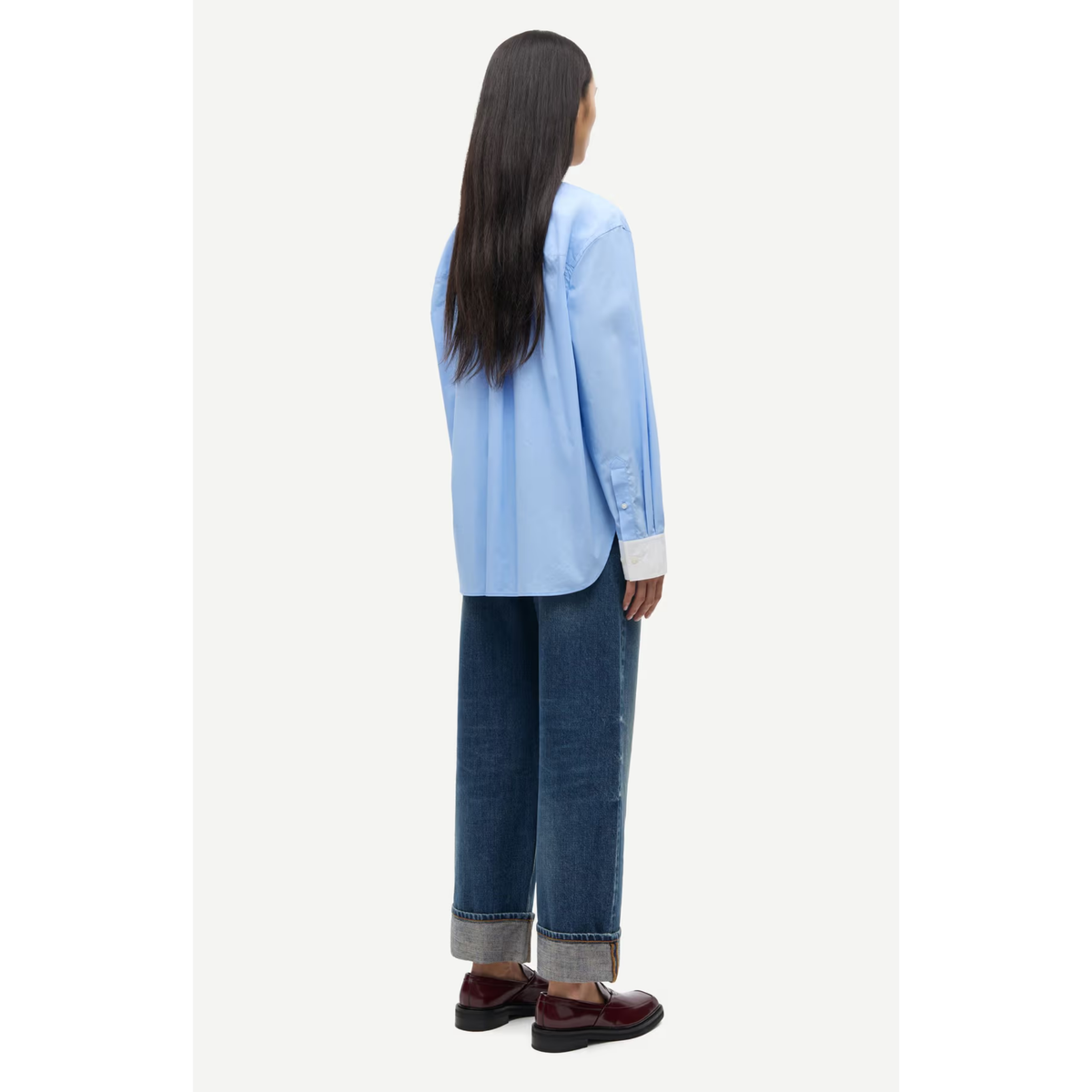 A model shown from the back wearing a light blue long-sleeve button-up shirt, dark blue wide-leg jeans, and dark red loafers, set against a plain off-white background.