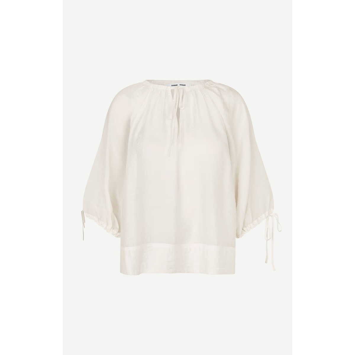 An off-white cotton blouse with a round neckline, gathered sleeves, and side ties, shown against a light gray background.