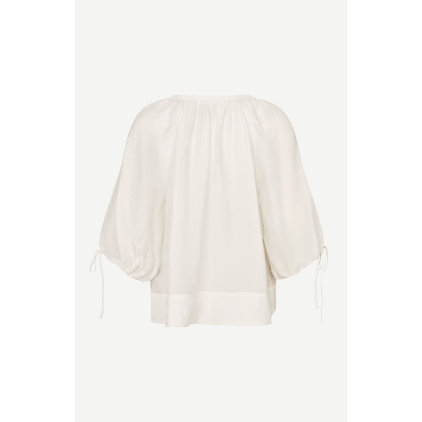 An off-white cotton blouse with a round neckline, gathered sleeves, and side ties, shown against a light gray background.