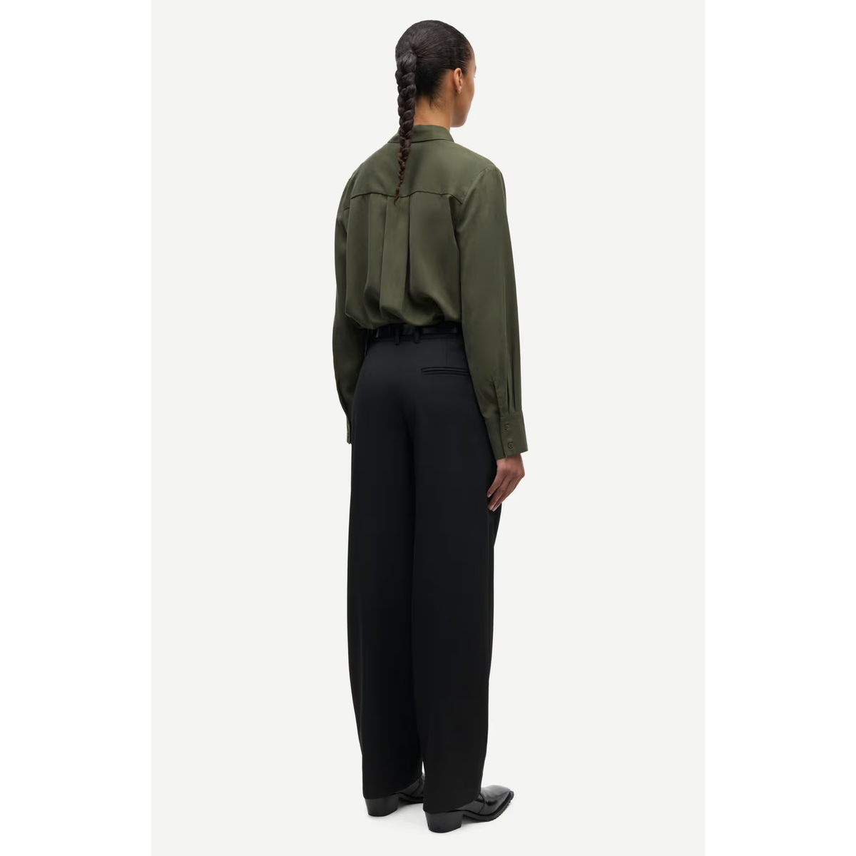 A model shown from the back wearing an olive green long-sleeve shirt and black wide-leg trousers, standing against a light gray studio background.