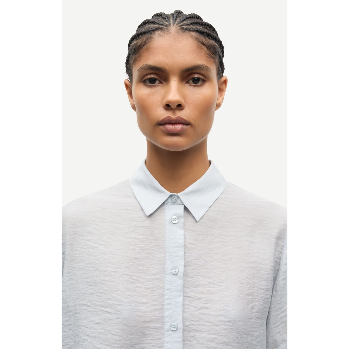 A model with braided hair wearing a light gray textured button-up shirt with a crisp white collar, shot against a solid off-white background.