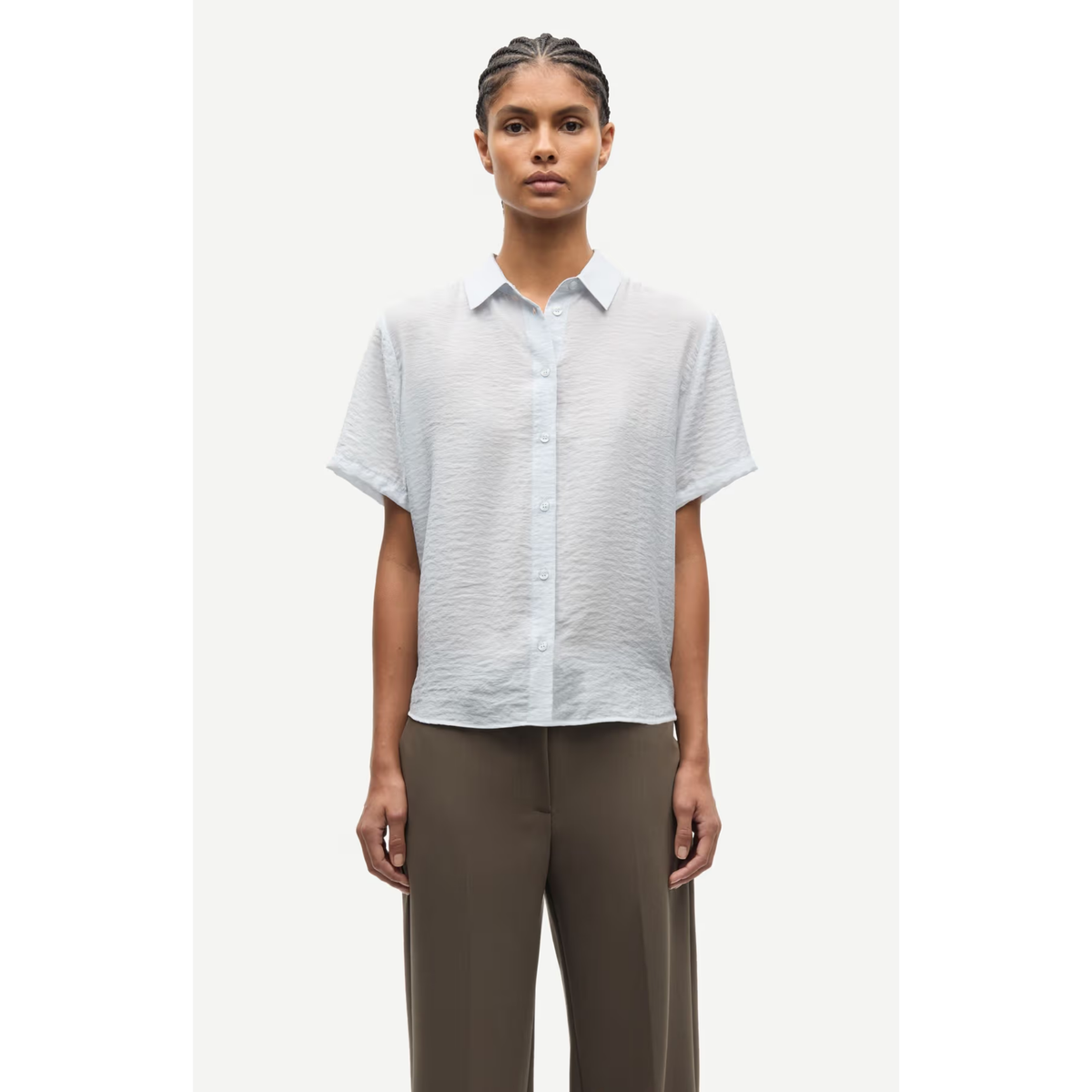 Woman wearing a light gray short-sleeve shirt and brown pants on a white background