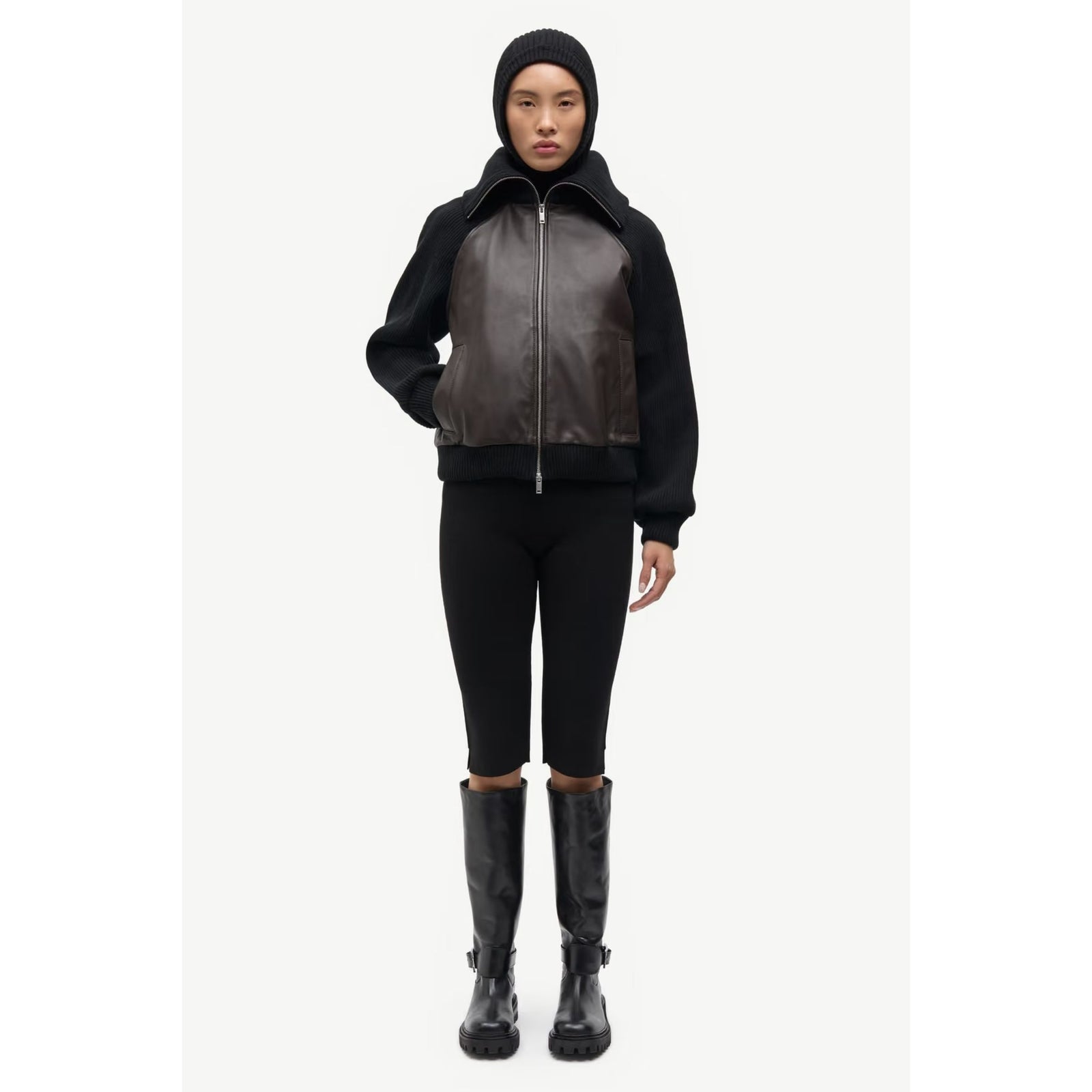 A cropped bomber-style jacket featuring dark brown faux-leather panels on the front and a black ribbed knit body, sleeves, and collar, shown against a light gray background.