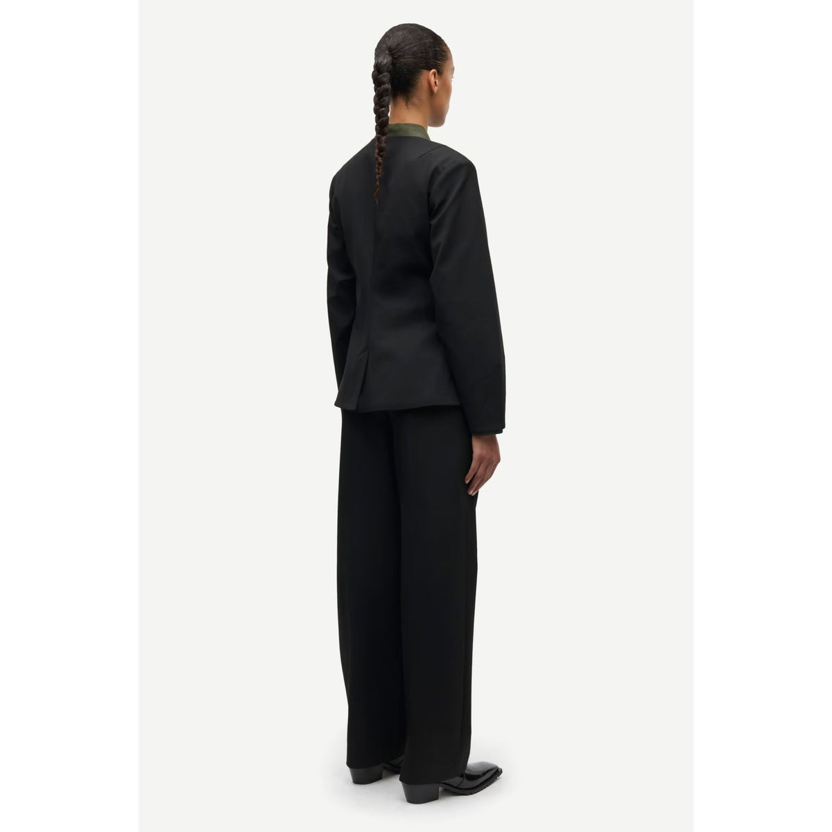 A model shown from the back wearing a black tailored suit with a structured jacket and wide-leg trousers, photographed against a plain light gray studio background.