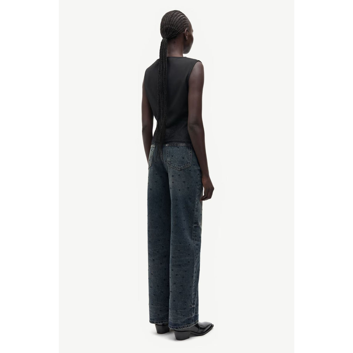 A model shown from the back wearing dark wide-leg jeans with a subtle star pattern, a black sleeveless top, and black studded shoes against a plain light background.