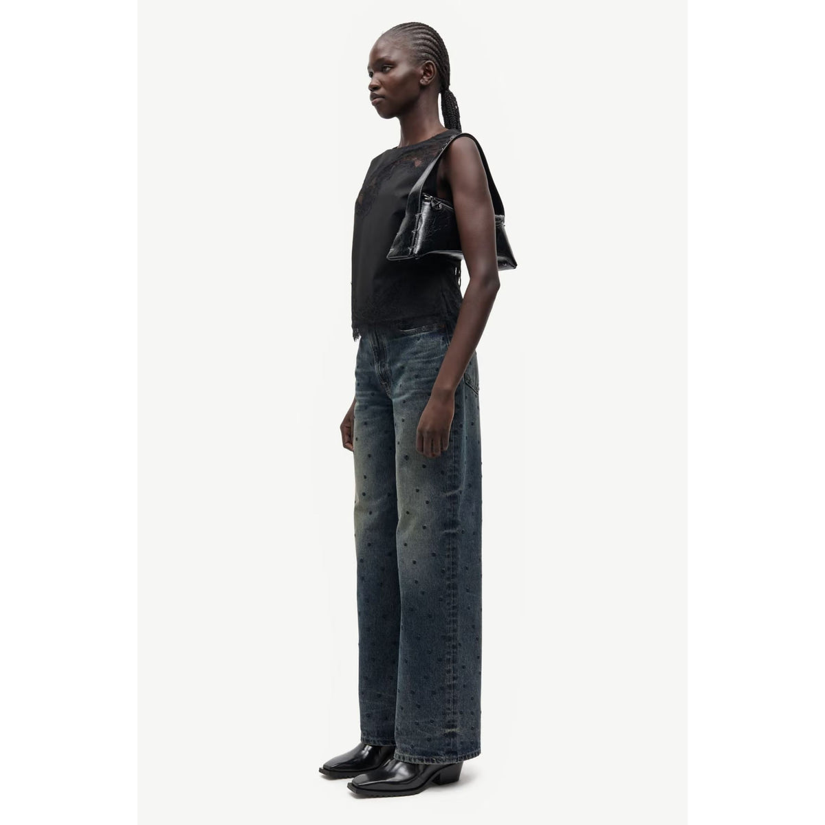 A woman modeling a sleeveless, high-neck maxi dress in a warm rust brown color, paired with black ankle boots, set against a plain white background.