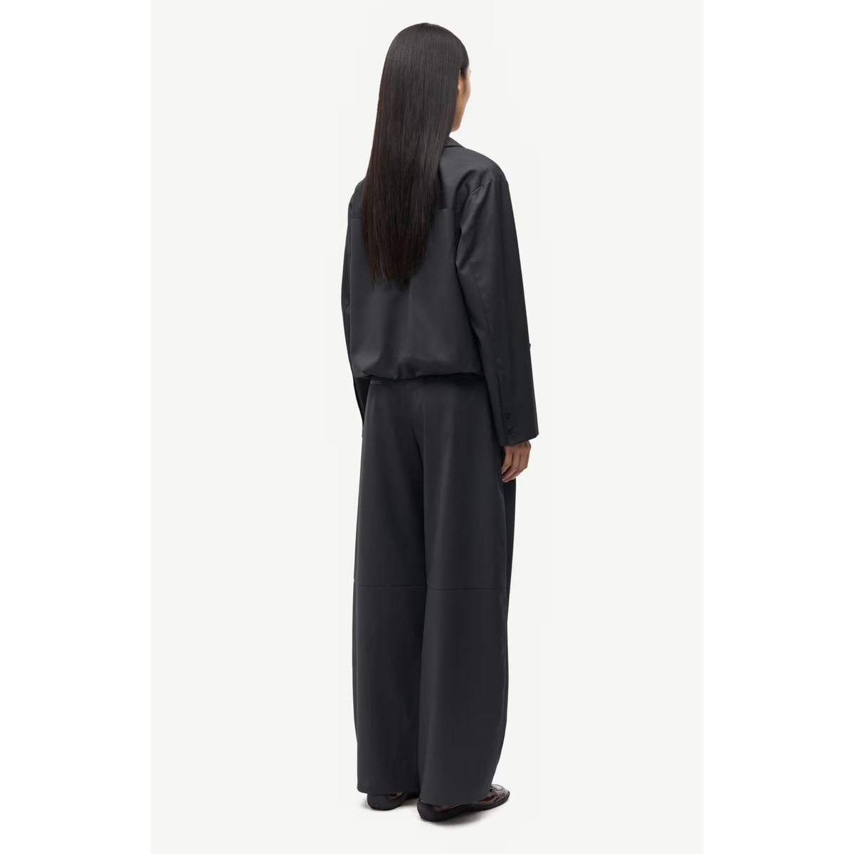 A model viewed from the back wearing a black satin-like long-sleeve top and matching wide-leg trousers against a plain white background.