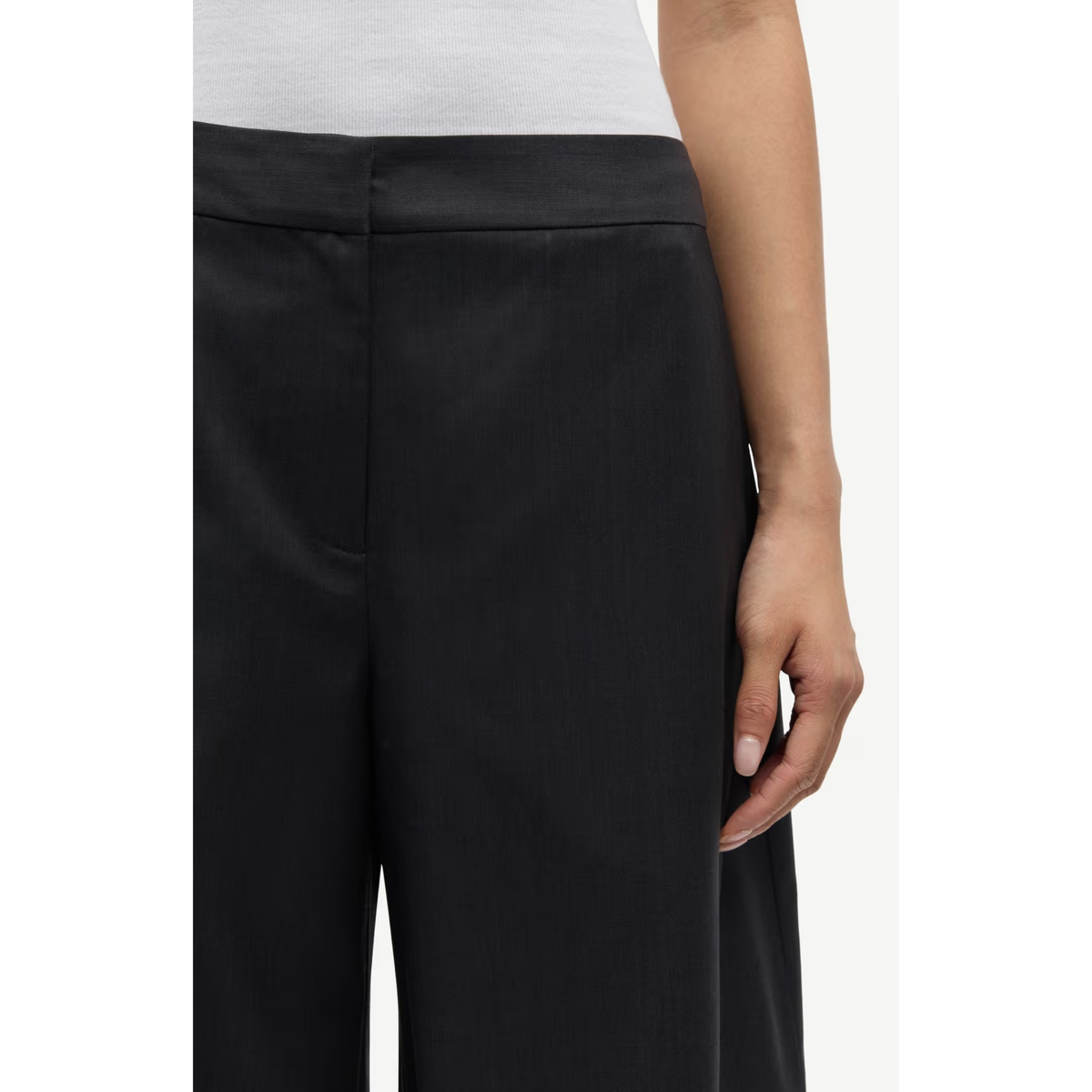 Close-up of a model wearing black wide-leg trousers with a high waistband, paired with a white top, shown against a plain white background.