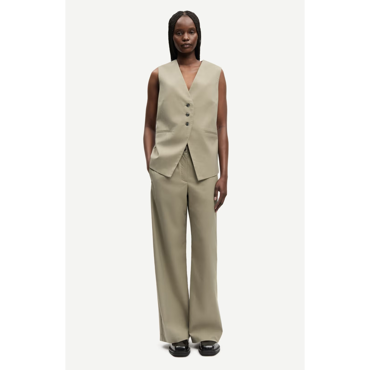 A model wearing a beige sleeveless vest and matching wide-leg trousers, standing against a light gray studio background.