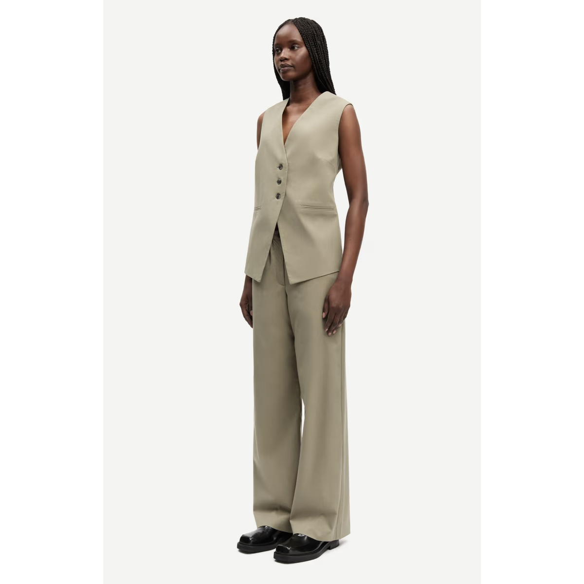 A model wearing a beige sleeveless vest and matching wide-leg trousers, styled with black loafers, against a light gray studio background.