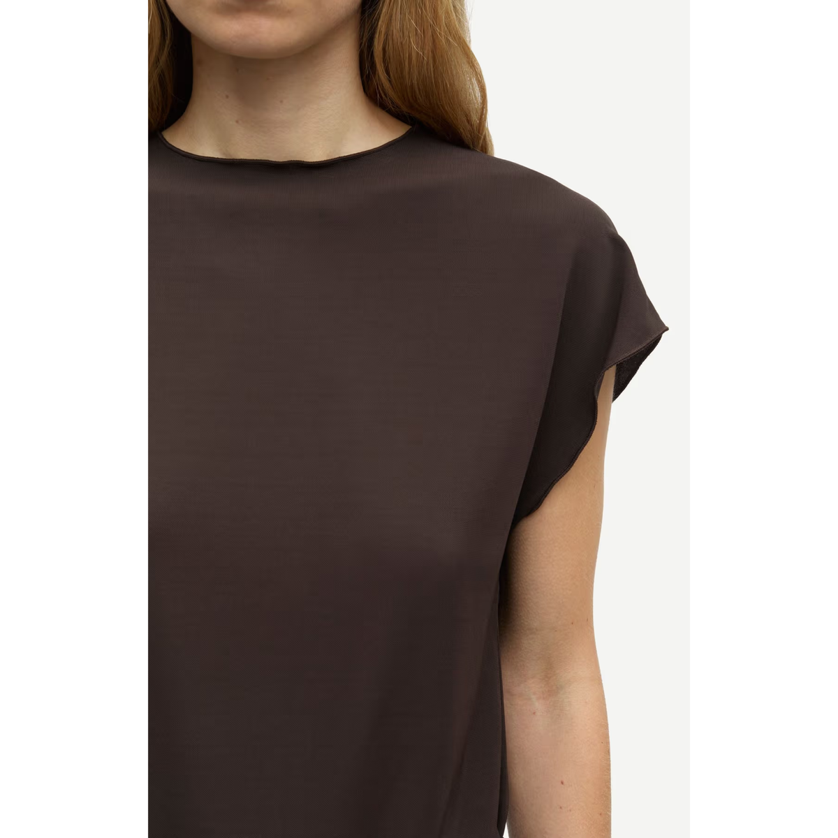 A close-up of a model wearing a dark brown short-sleeve top with a crew neckline, set against a plain off-white background.