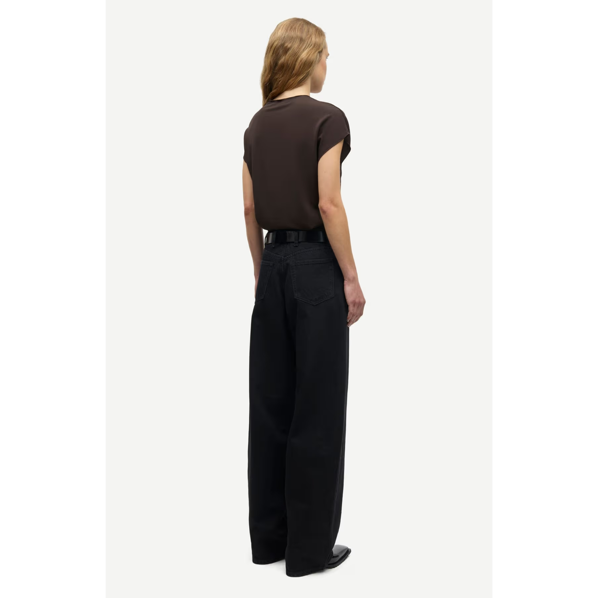 A model shown from the back wearing a dark brown short-sleeve t-shirt, black wide-leg trousers, and black shoes, standing against a light gray studio background.