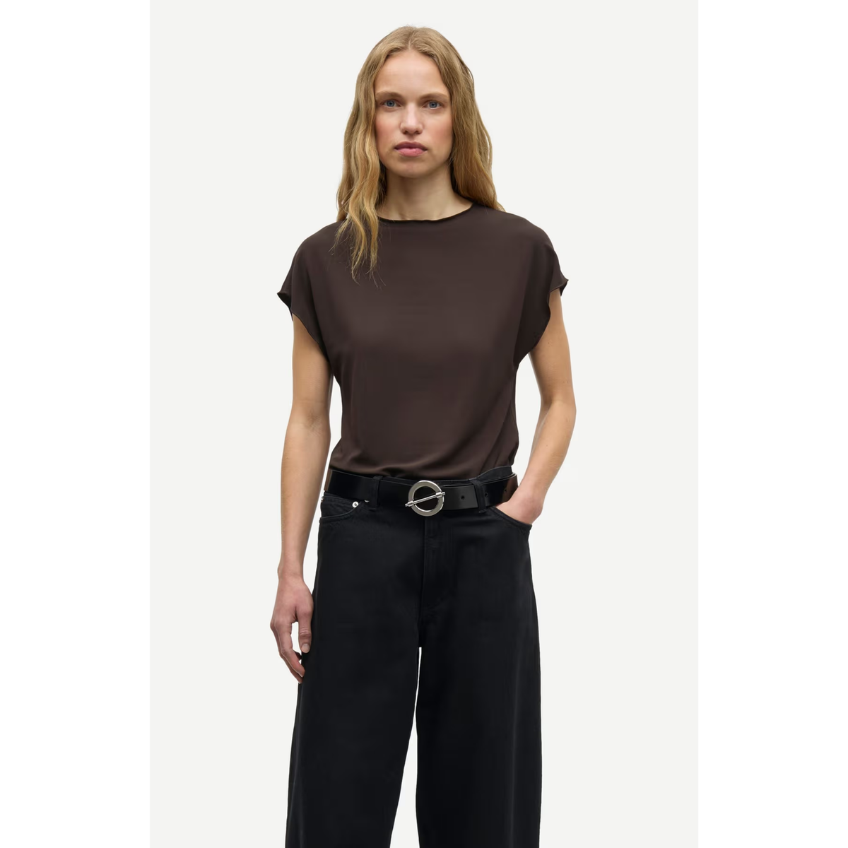 A woman modeling a dark brown short-sleeve top with black wide-leg trousers and a black belt, set against a plain light gray background.