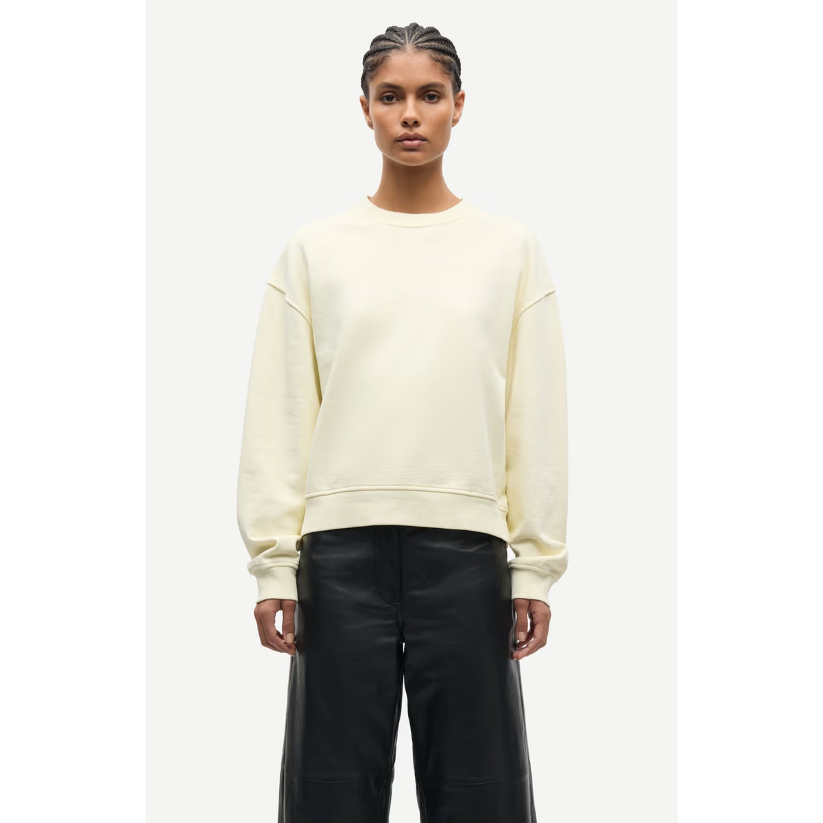 Person wearing a light-colored sweatshirt and black pants on a white background