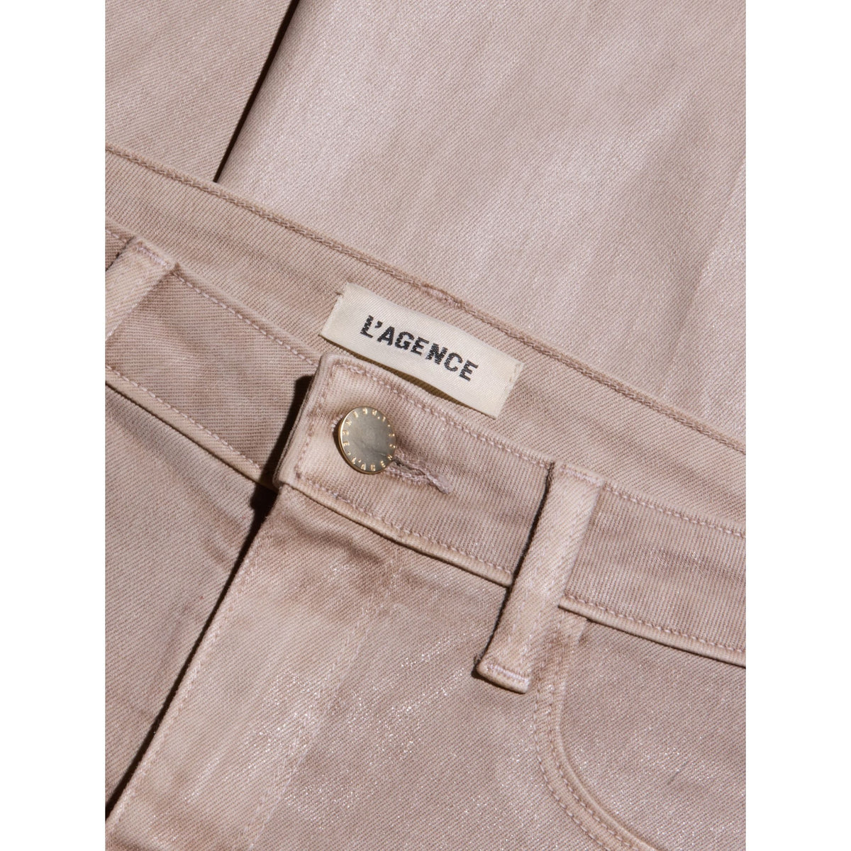 Close-up of a pair of light beige trousers showing the waistband, belt loop, button, and a visible L'AGENCE brand label.