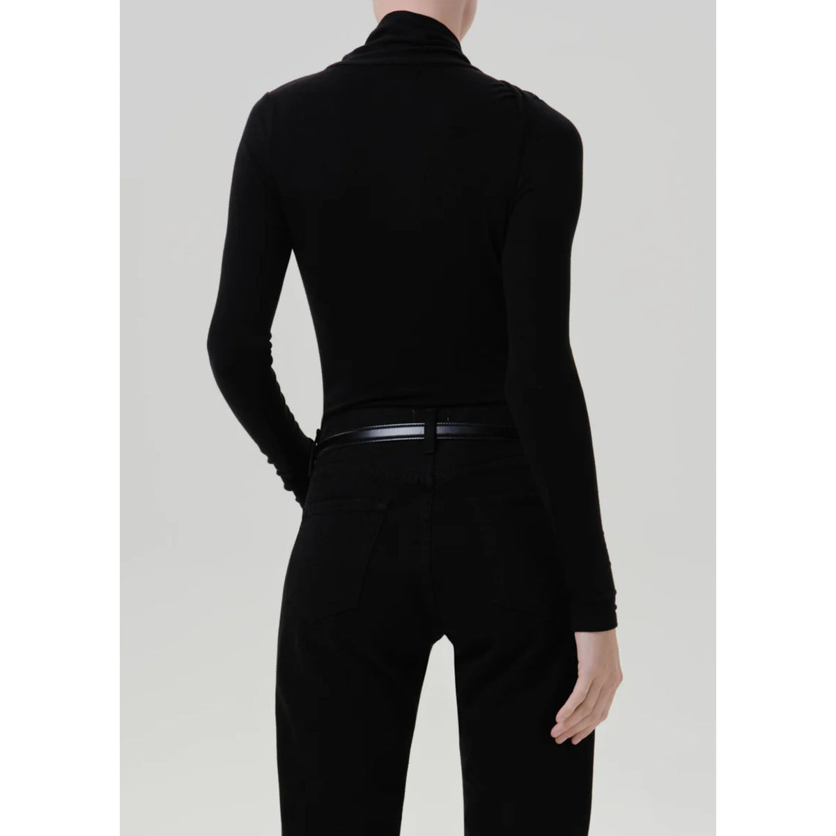 A model shown from the back wearing a black long-sleeve mock neck top and black pants against a light gray studio background.