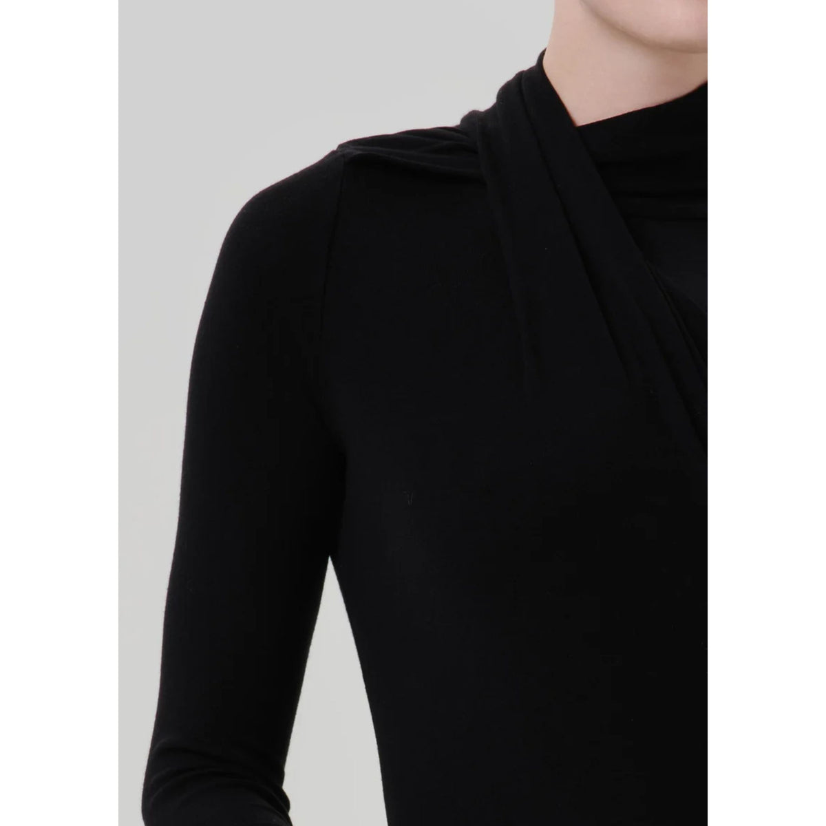 Close-up of a model wearing a black long-sleeve top with a draped, asymmetrical neckline against a light gray background.