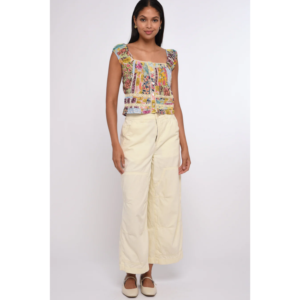 Woman wearing a colorful top and cream pants on a white background