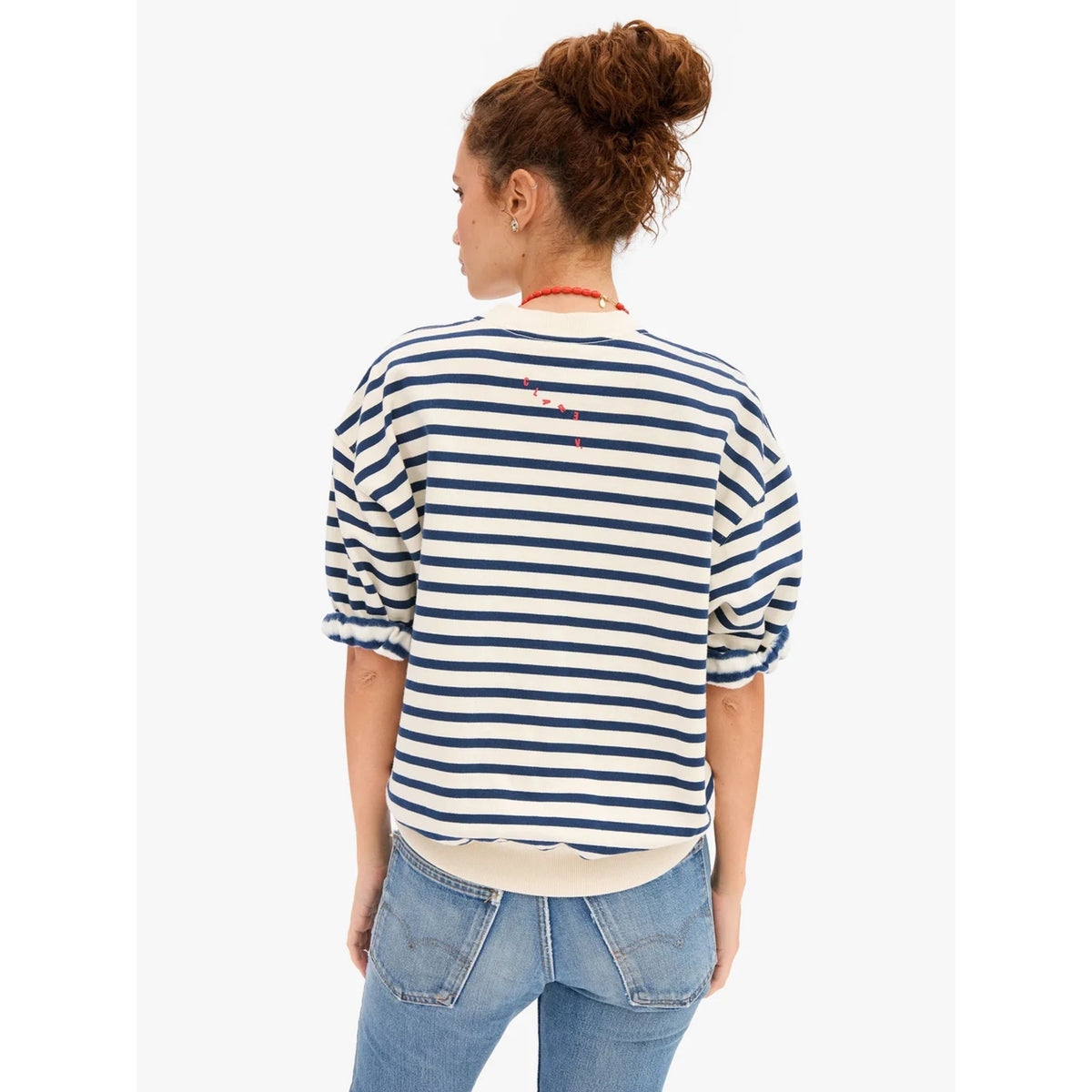Back view of a model wearing the cream and navy striped short-sleeve oversized sweatshirt styled with light-wash denim jeans.