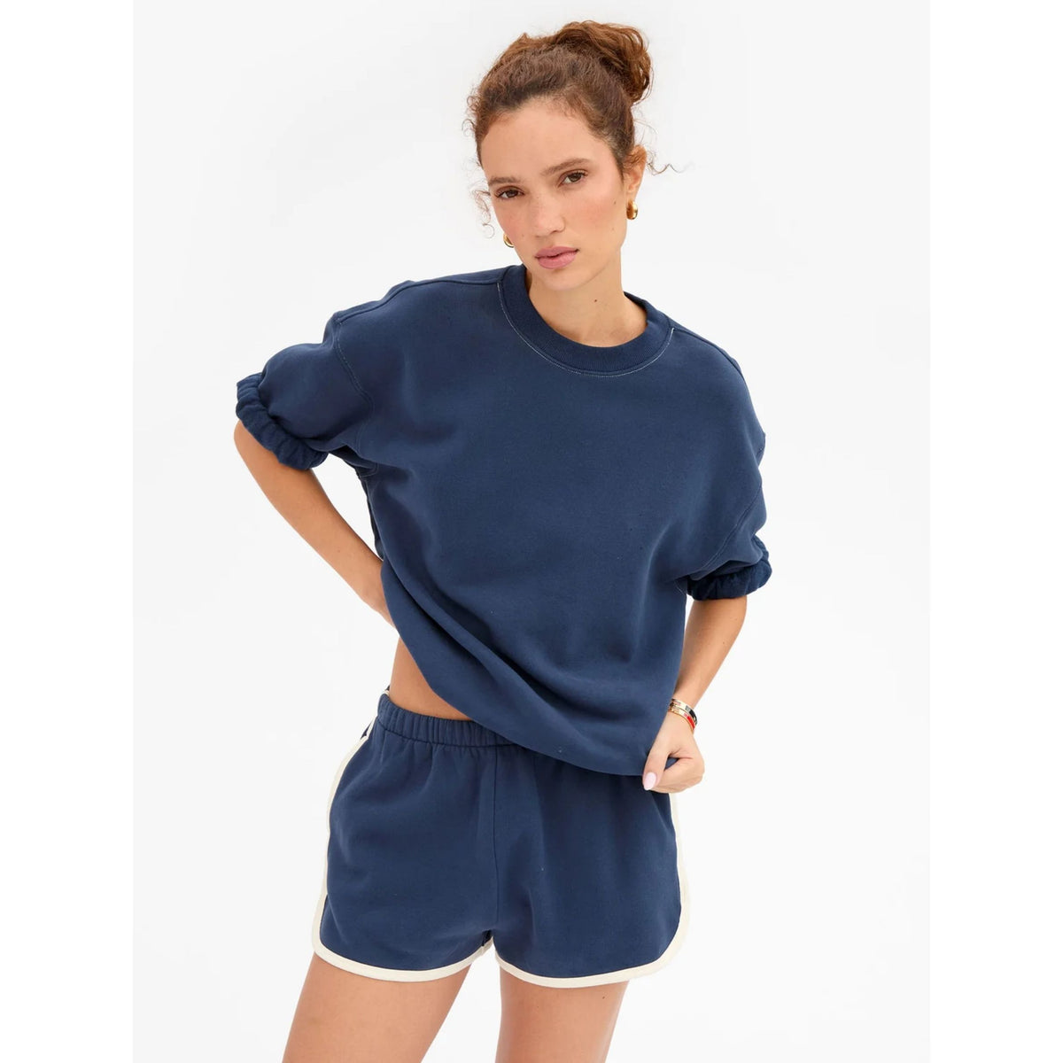 Three-quarter waist-up shot of a model posing in the solid navy short-sleeve oversized sweatshirt and matching shorts with hand on hip.