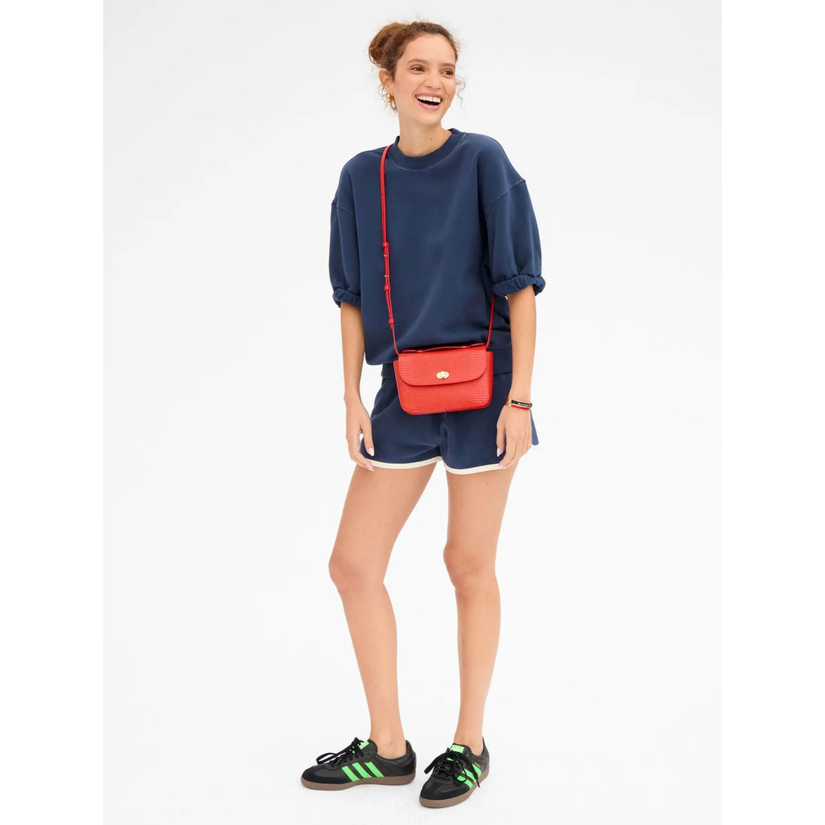 Full-length front view of a model wearing the solid navy short-sleeve oversized sweatshirt set styled with a red crossbody bag and sneakers.