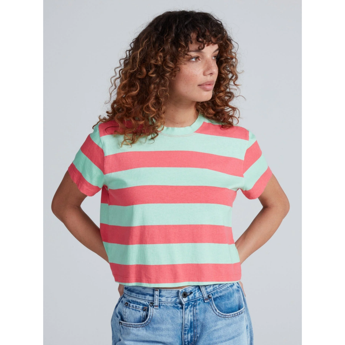 Woman wearing a red and green striped shirt with blue jeans on a light gray background