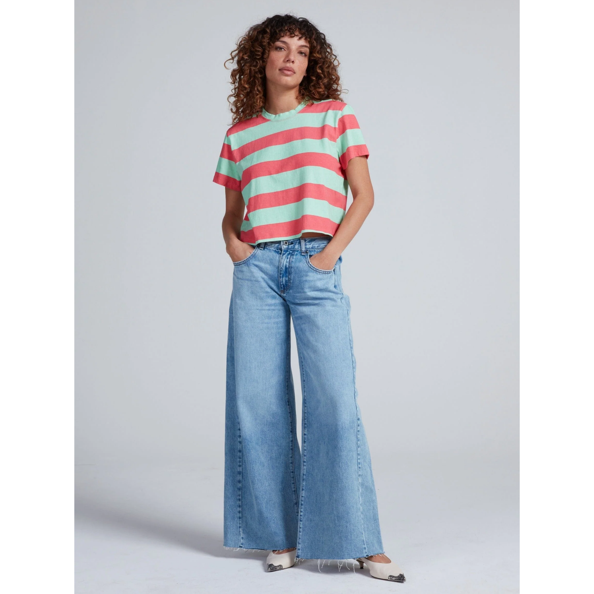 Woman wearing a striped shirt and wide-leg jeans against a plain background