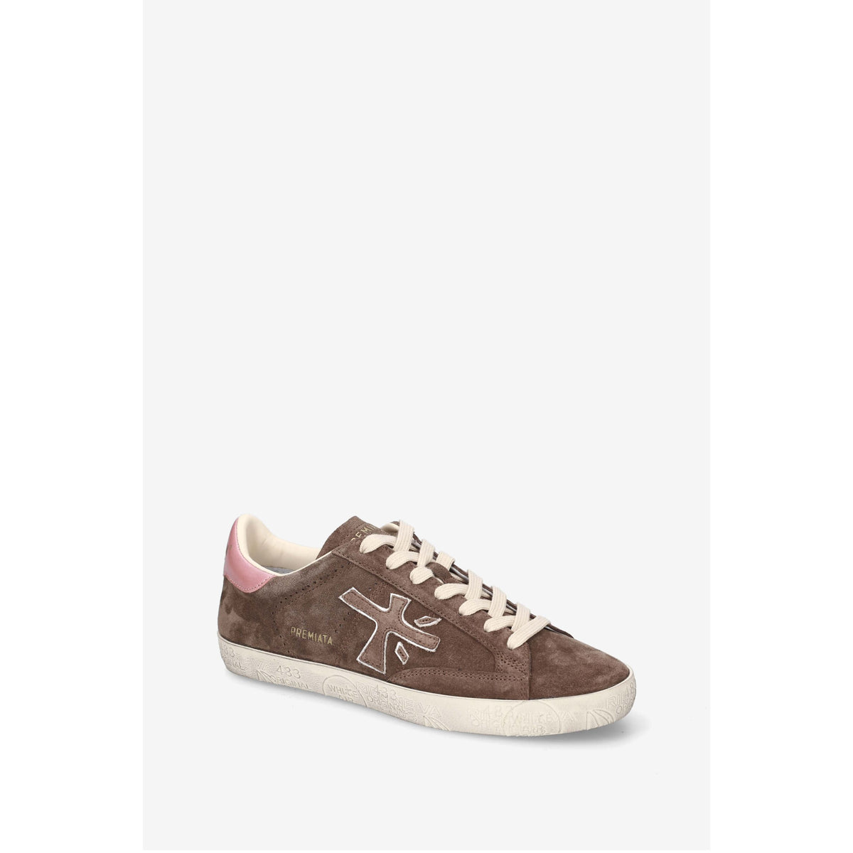 A brown suede sneaker with a pink heel tab, cream laces, and a cream rubber sole, shown against a light gray background.