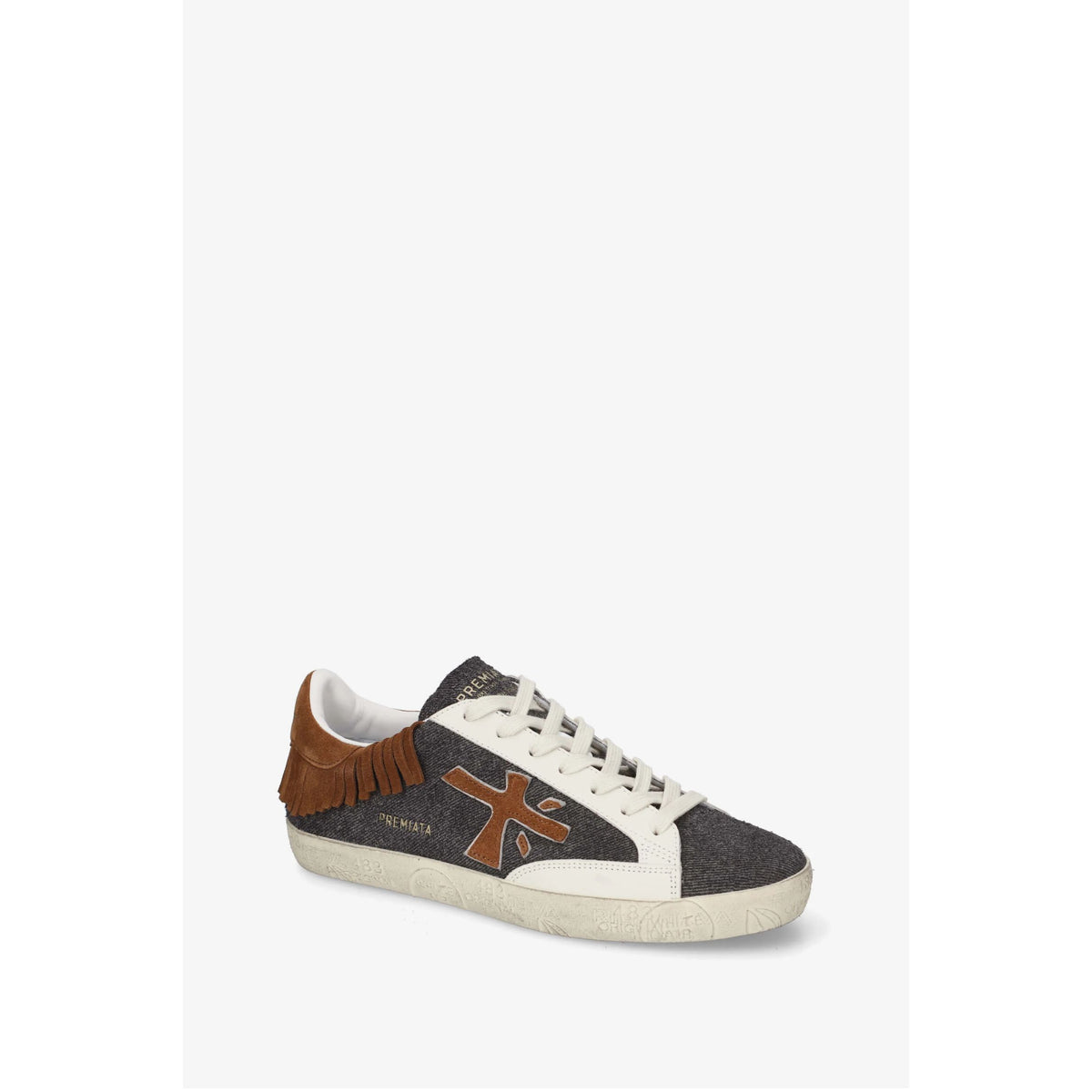 A single low-top sneaker by PREMIATA, featuring a dark gray woven upper, brown suede fringe detail along the collar, a brown cross-shaped logo on the side, white laces, and a white rubber sole, shown against a plain light gray background.