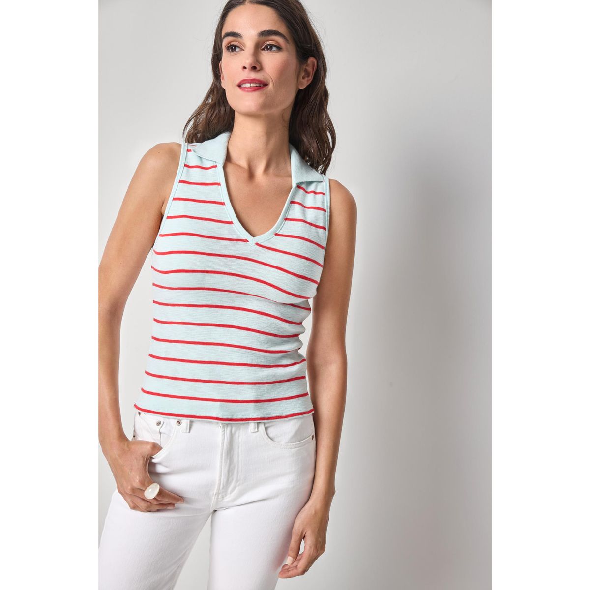 Woman wearing a light blue sleeveless top with red stripes and white pants on a plain background