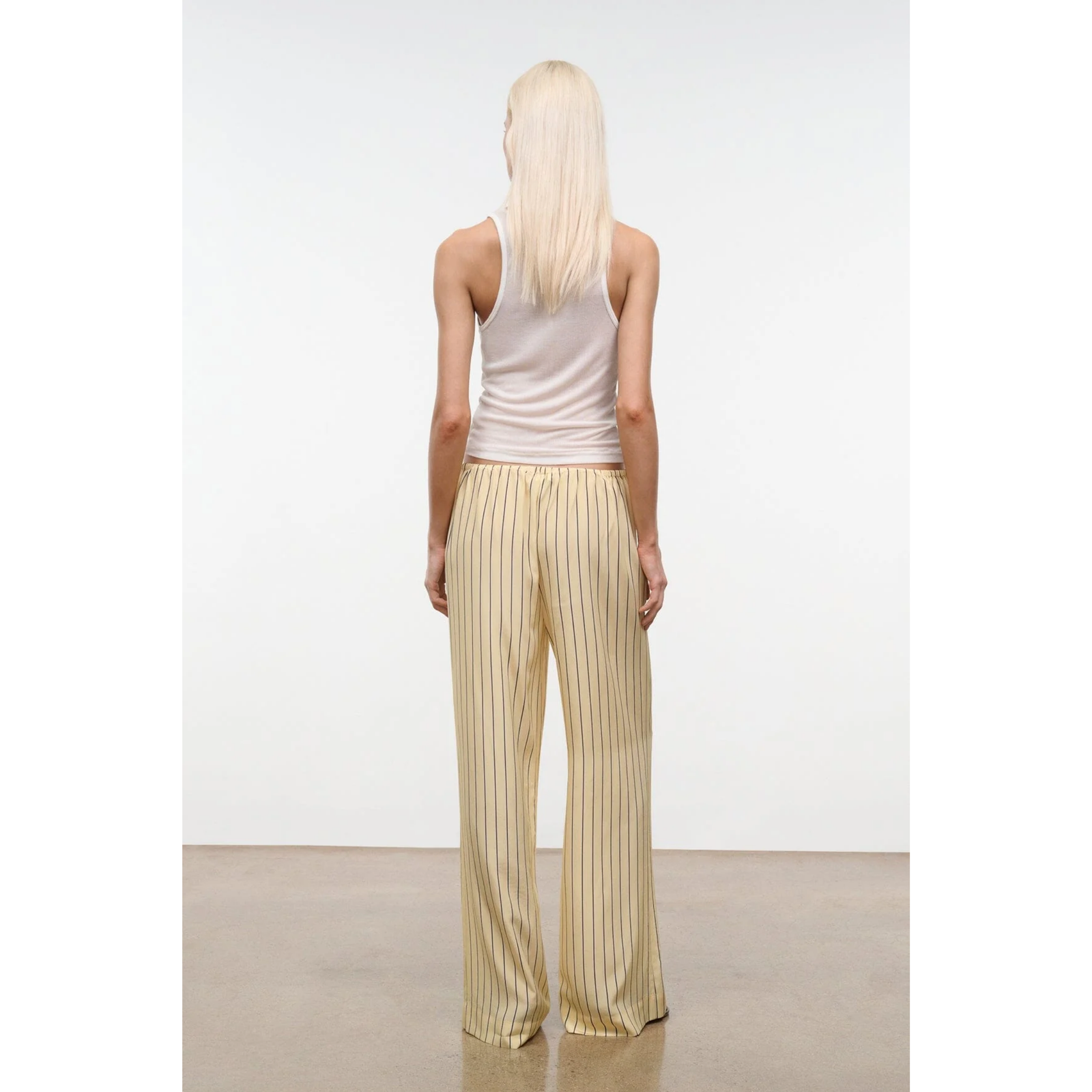 Woman wearing a white tank top and beige striped pants against a plain background