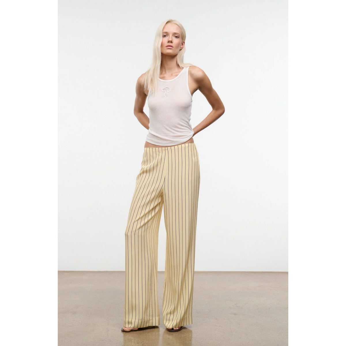 Woman wearing a white tank top and beige striped pants against a plain background