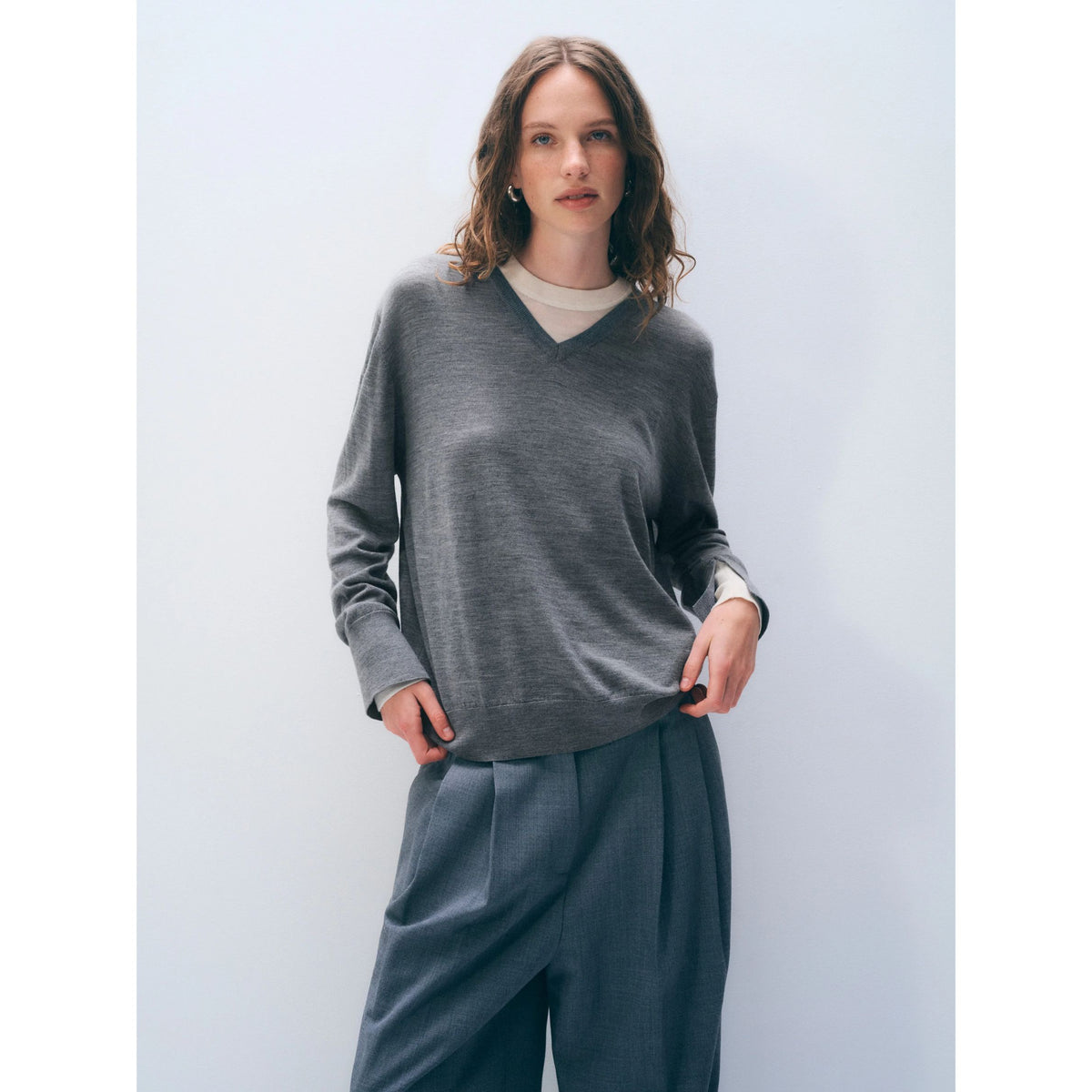 Waist-up shot of a model wearing the grey layered v-neck sweater paired with dark grey trousers.
