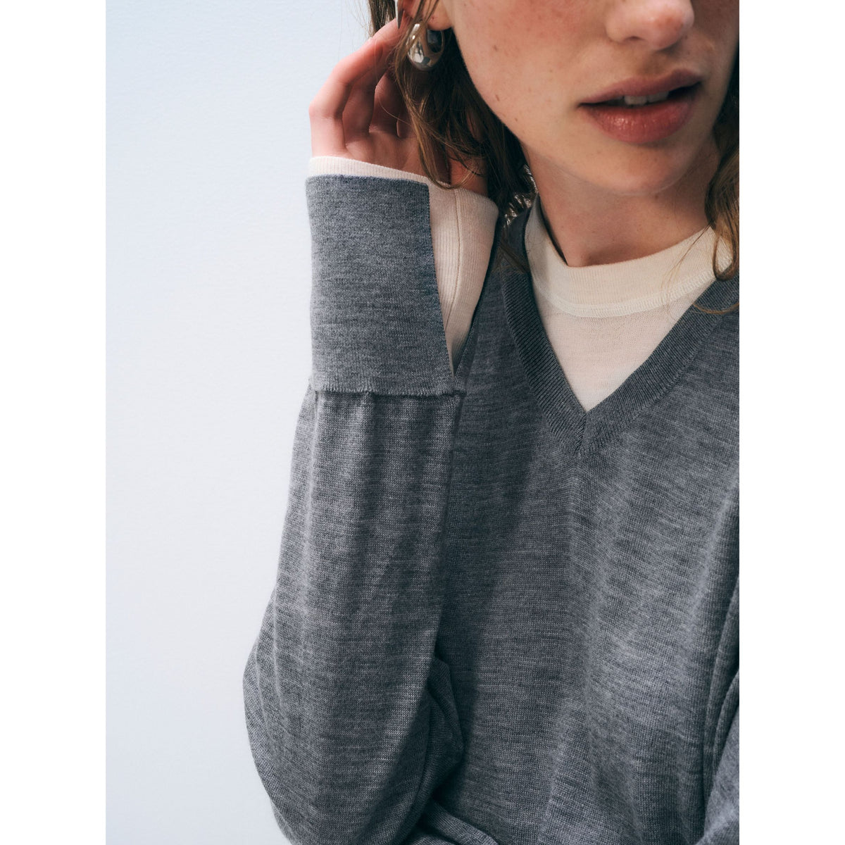 Close-up shot of a model wearing the grey layered v-neck sweater, highlighting the cuff and sleeve detail.