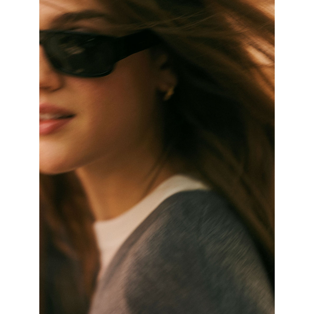 Outdoor close-up shot of a model wearing sunglasses and the grey layered v-neck sweater.