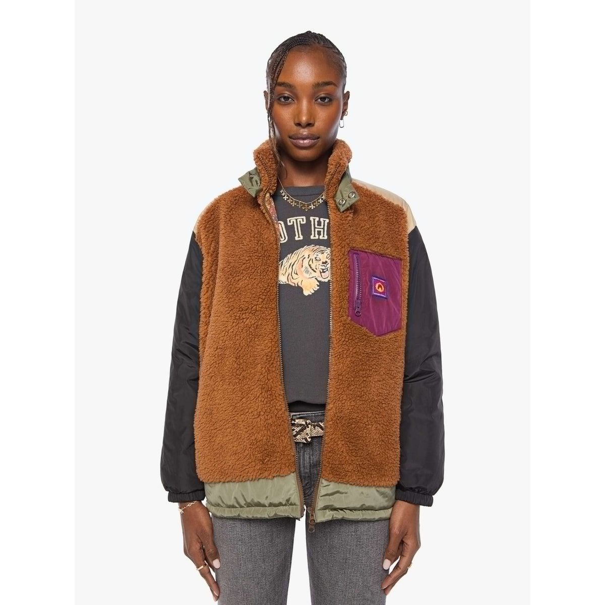 A model wearing a brown sherpa-lined puffer vest with black sleeves, olive green trim, and a purple chest pocket with a red logo patch, layered over a tiger-print graphic tee and gray jeans.