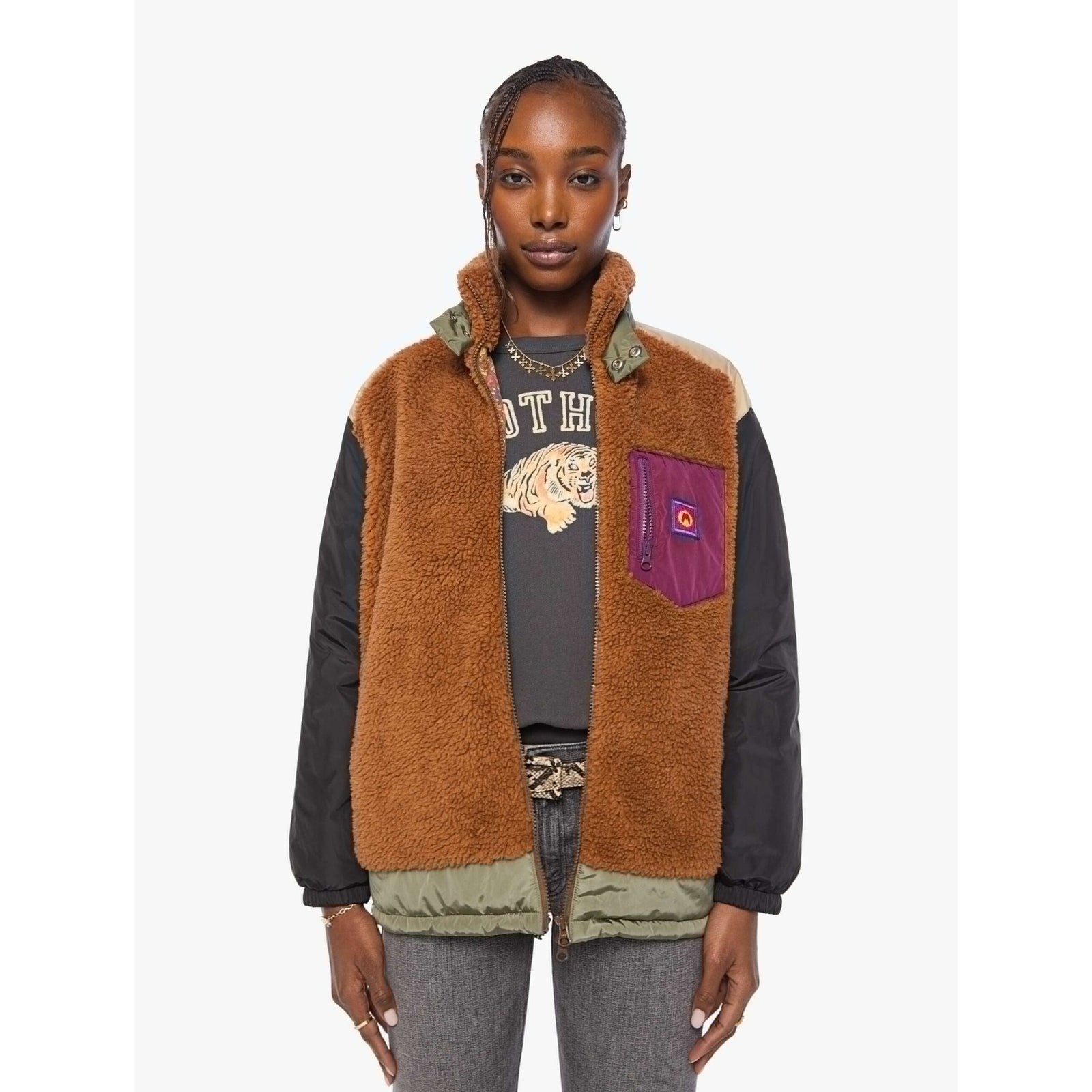 A model wearing a brown sherpa-lined puffer vest with black sleeves, olive green trim, and a purple chest pocket with a red logo patch, layered over a tiger-print graphic tee and gray jeans.
