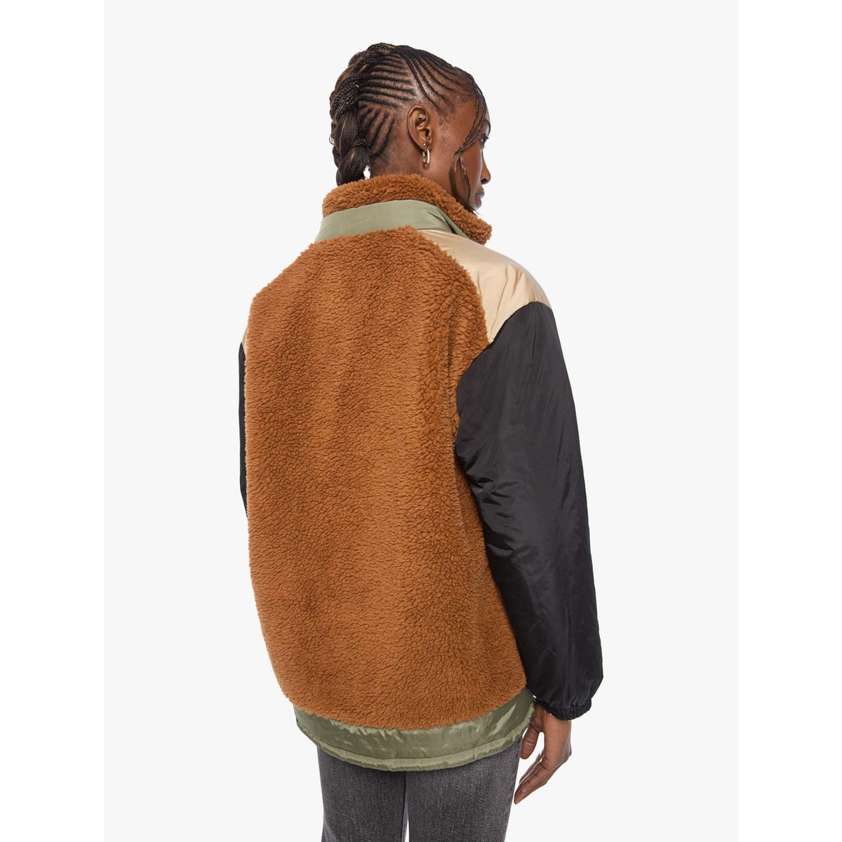 A person shown from the back wearing a color-blocked fleece jacket with a brown sherpa back panel, beige shoulder panels, and black sleeves, against a plain light background.
