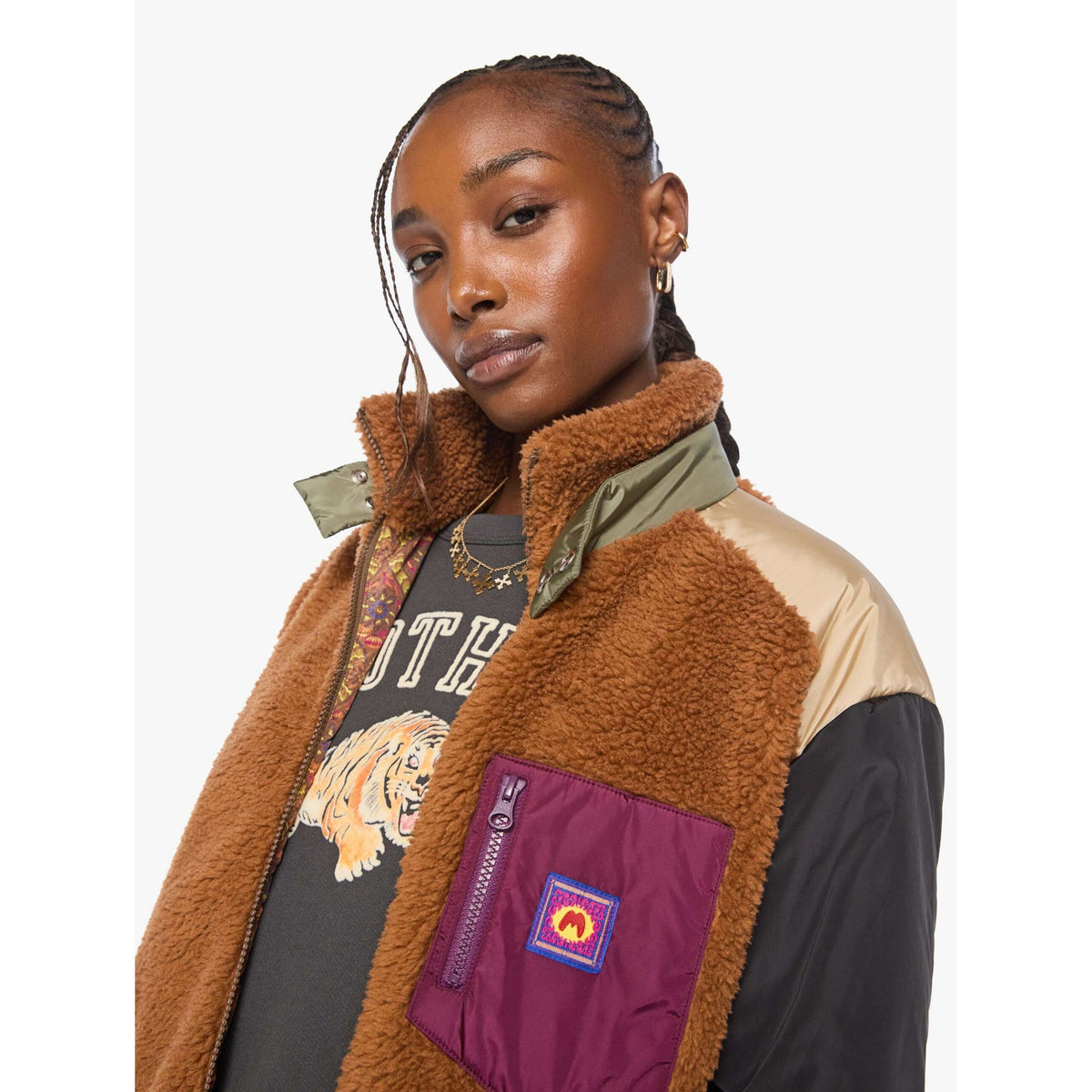 A model wearing a colorblock fleece jacket with brown sherpa lining, beige and black panels, and a purple chest pocket featuring a patch.