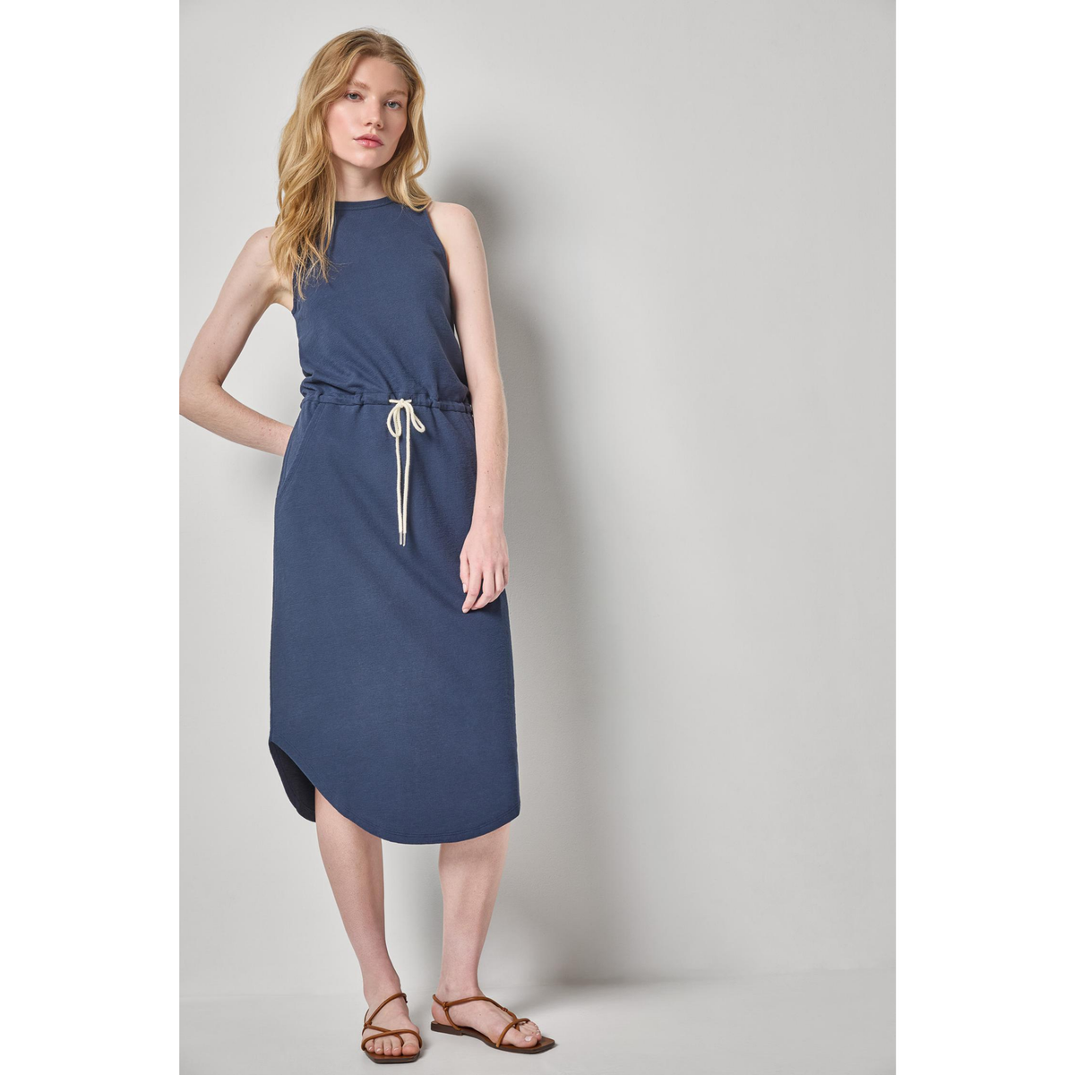 Woman wearing a blue sleeveless dress against a plain background