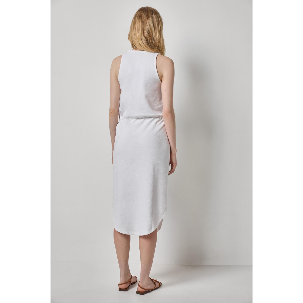 Woman wearing a white sleeveless dress against a plain background