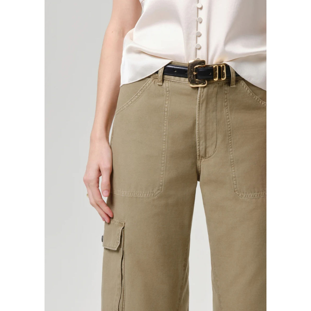 A close-up of a person wearing high-waisted khaki cargo pants with a black belt featuring a gold buckle, paired with a cream-colored blouse.